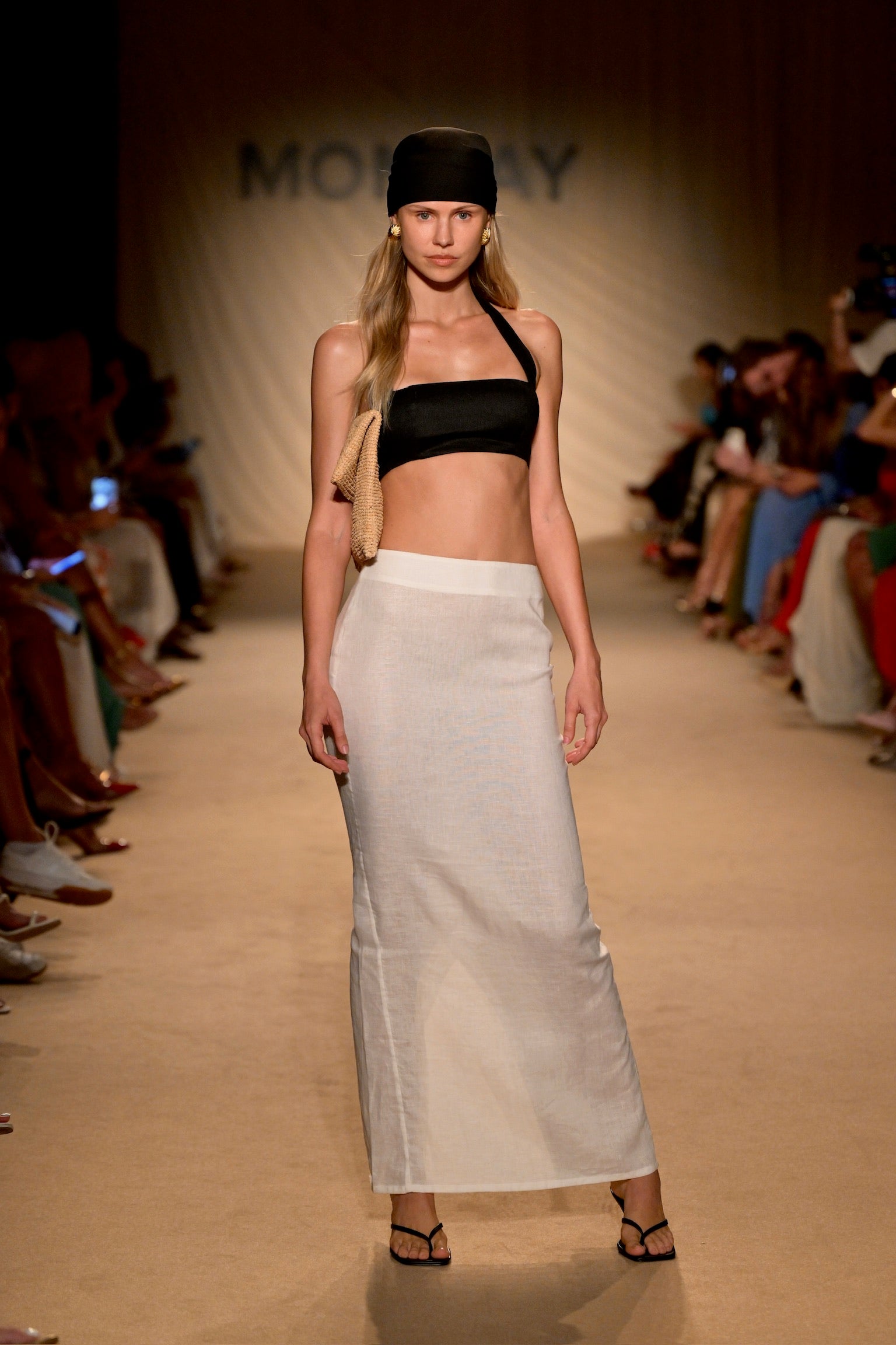Runway model in black bandeau top, white straight maxi skirt, black headscarf and sandals; 'MONDAY' logo on backdrop.