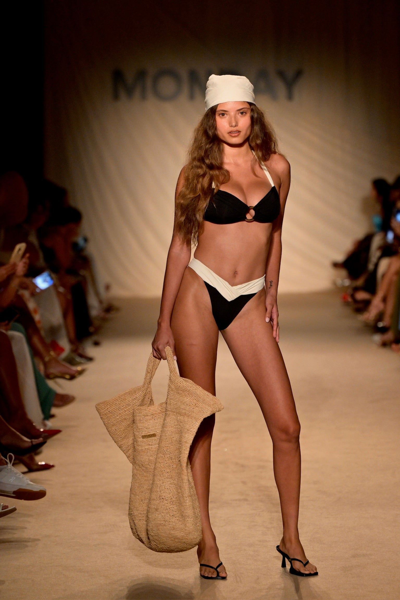 Runway model wearing black and ivory Bronte top and matching bottoms, white headscarf and straw tote; backdrop reads MONDAY