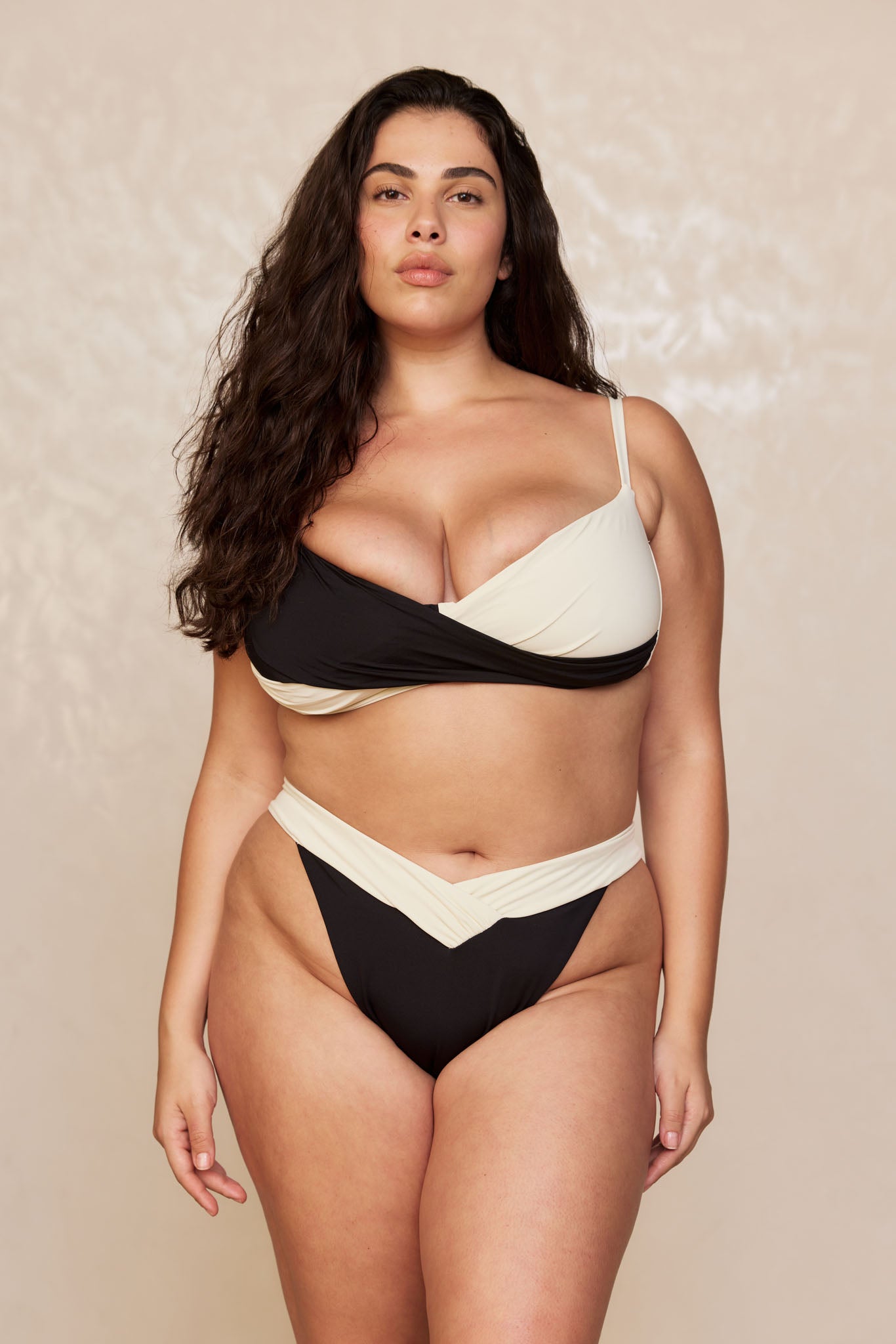 Woman wearing two-tone black and cream bikini with wrap-style top and high-cut bottoms, standing against a neutral backdrop.