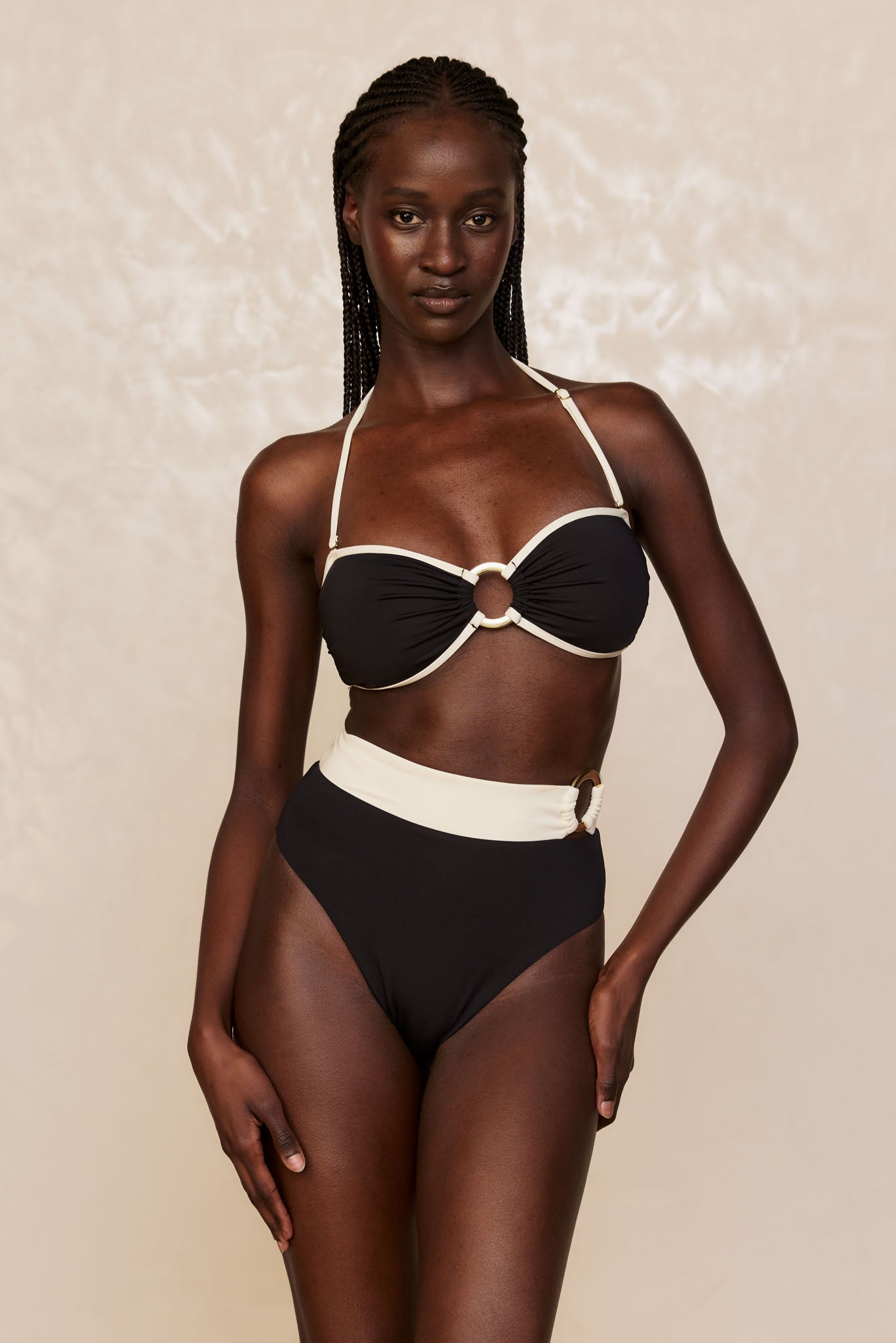 Black bandeau bikini with cream trim, ring at center and matching high-waist bottoms with side ring, modeled front view.
