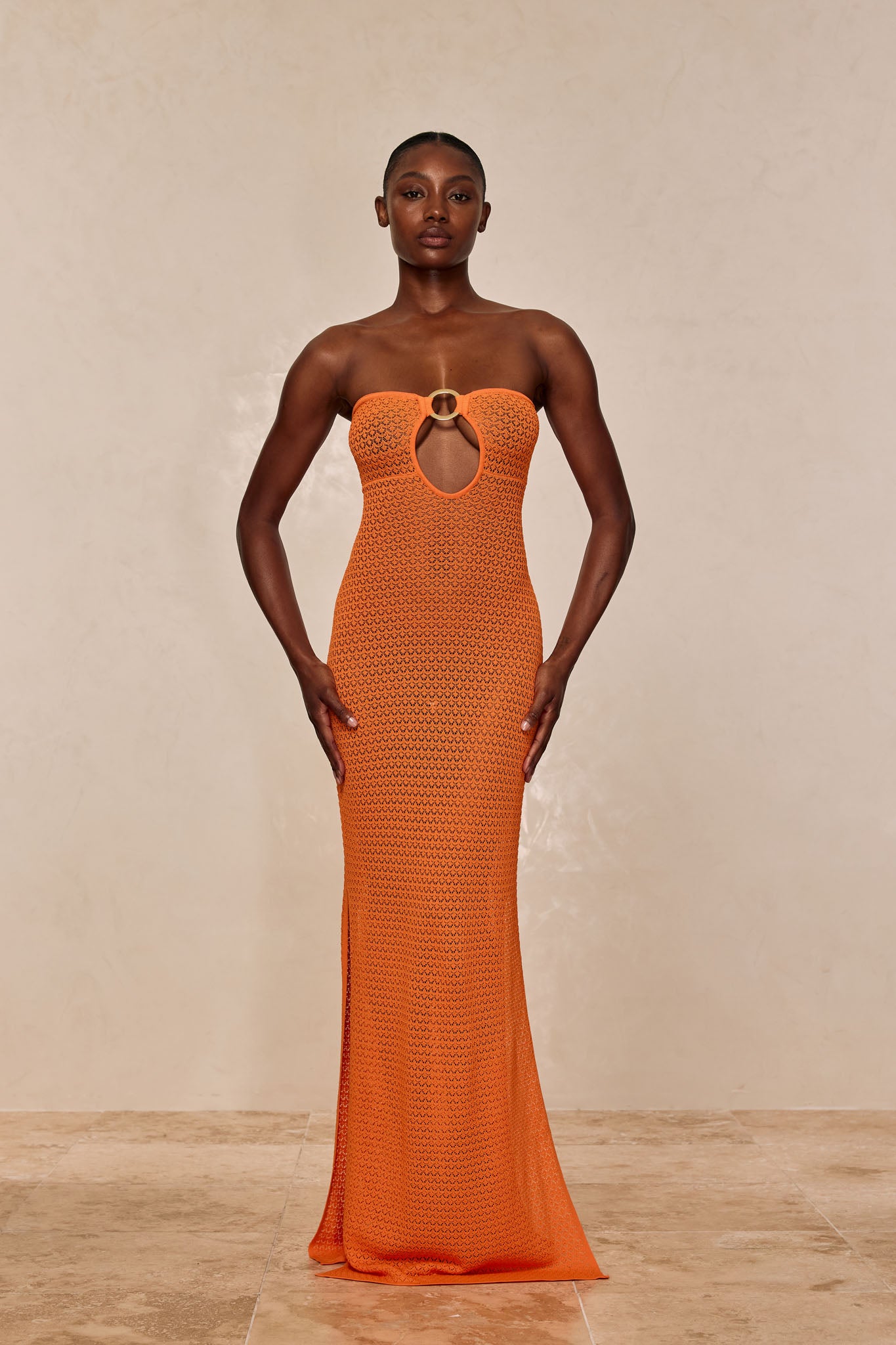 Model wearing a strapless orange crochet floor-length dress with a circular ring detail and front keyhole cutout