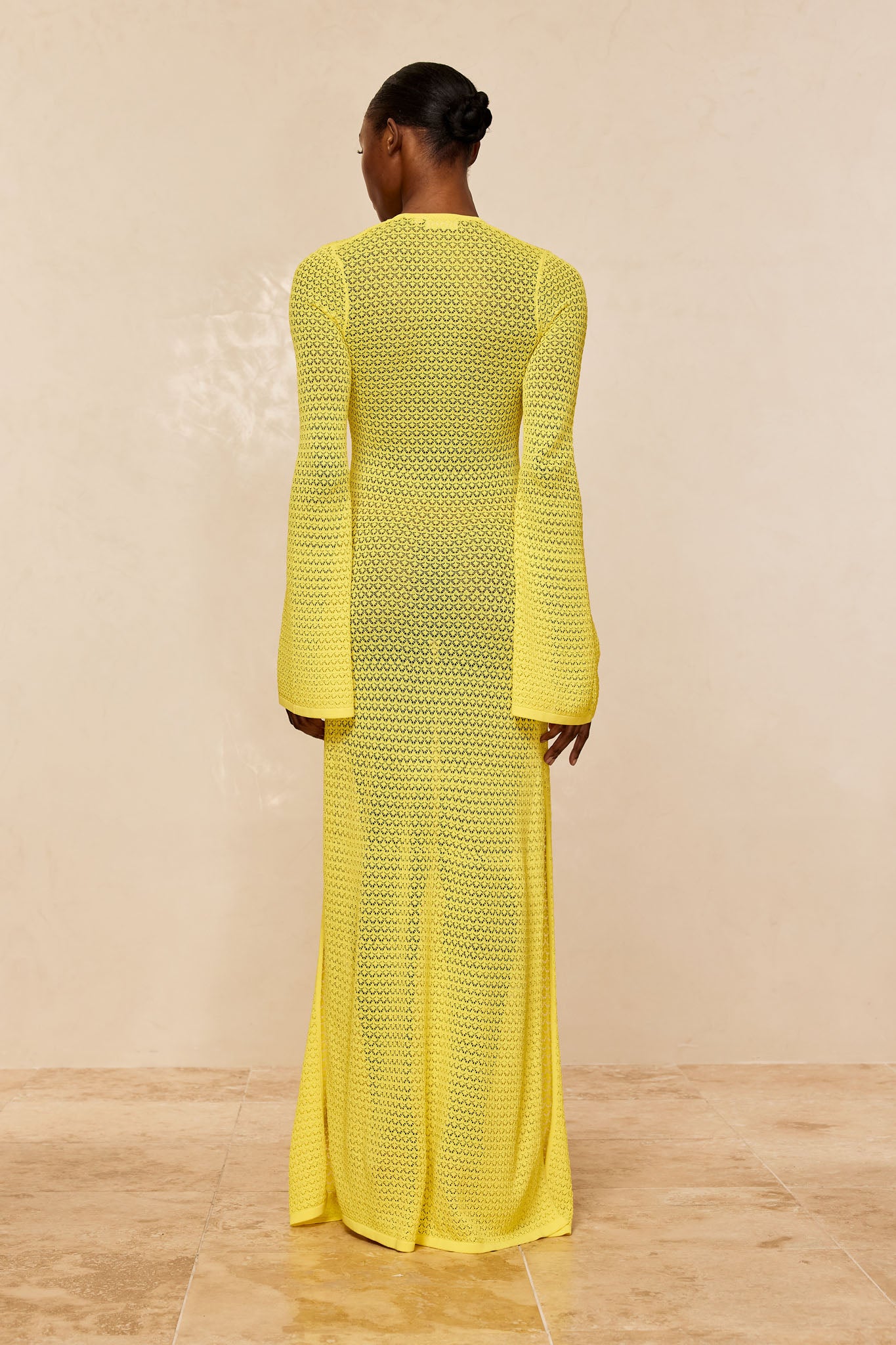 Back view of model wearing floor-length yellow open-knit long-sleeve dress with flared cuffs