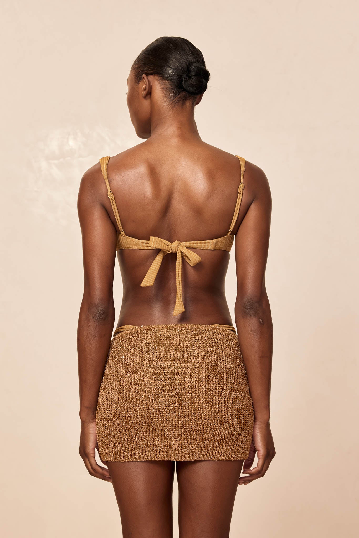 Rear view of woman wearing a mustard bikini top tied in a bow and a brown knit mini skirt