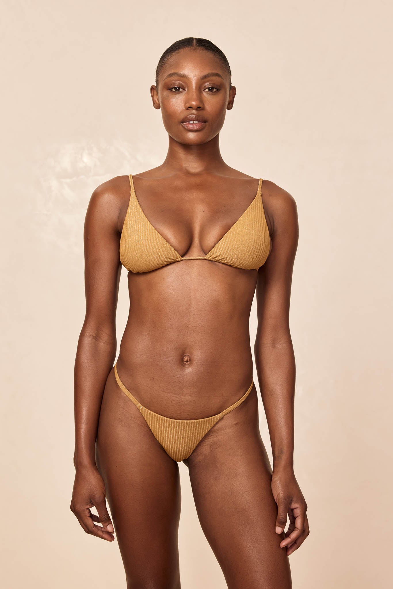 Model wearing tan ribbed triangle bikini, front view on beige backdrop.