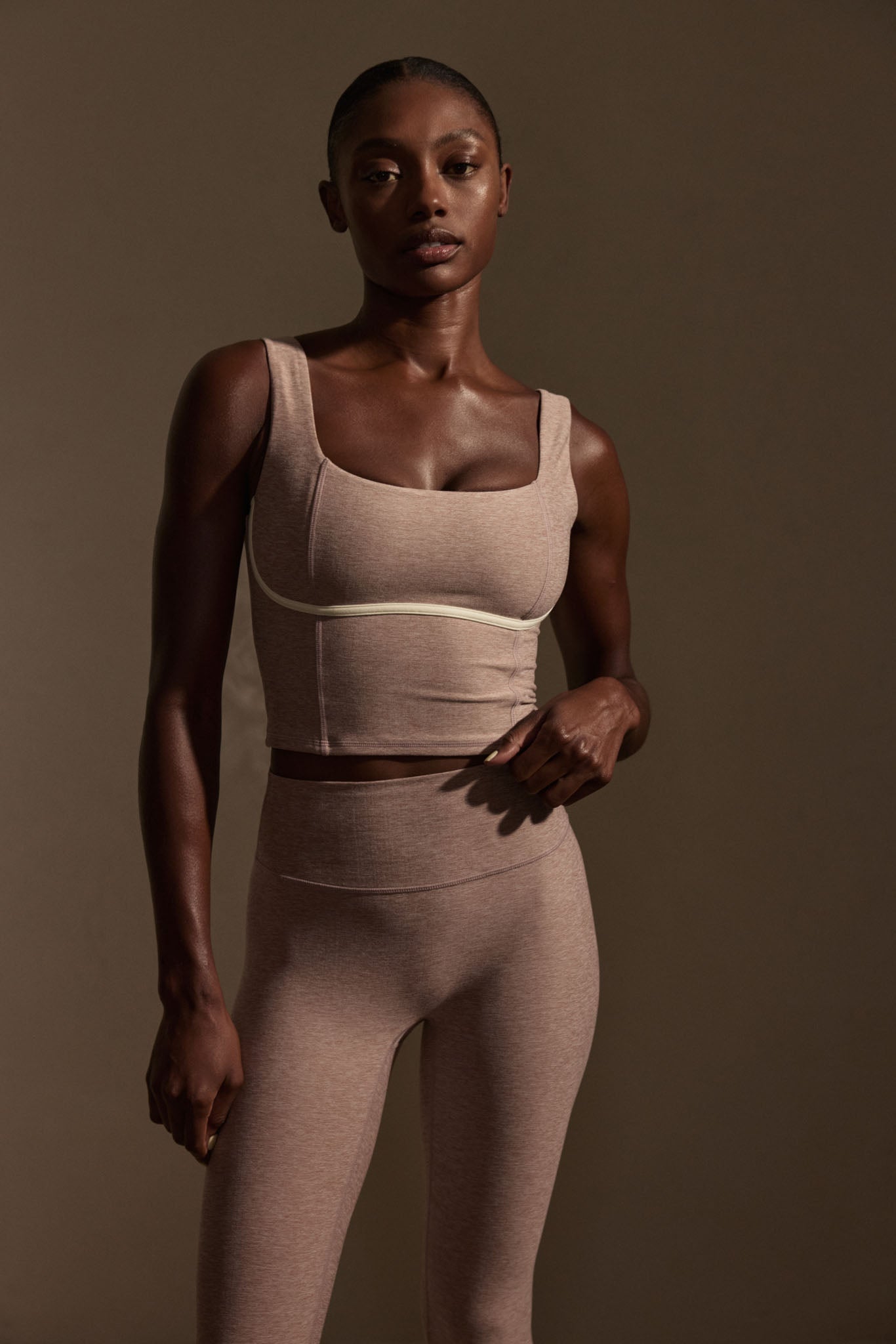 Woman modeling mauve crop tank and high-waist leggings, standing against a plain brown background.
