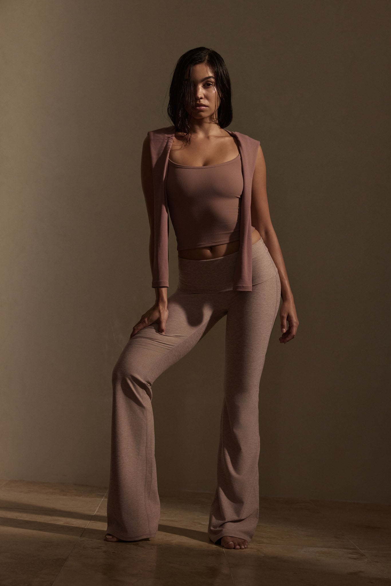 Woman standing full-length in mauve ribbed tank top, sleeveless shrug and wide-leg pants against a neutral studio background.