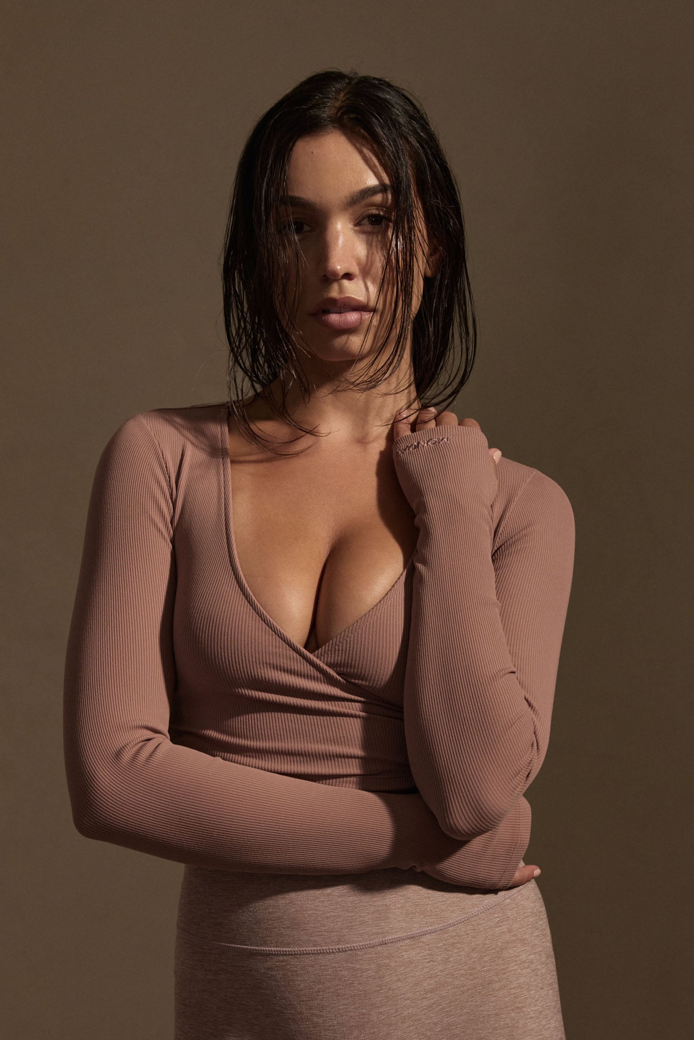 Woman with wet hair wearing a mauve ribbed wrap top and matching skirt, arms crossed against neutral background.