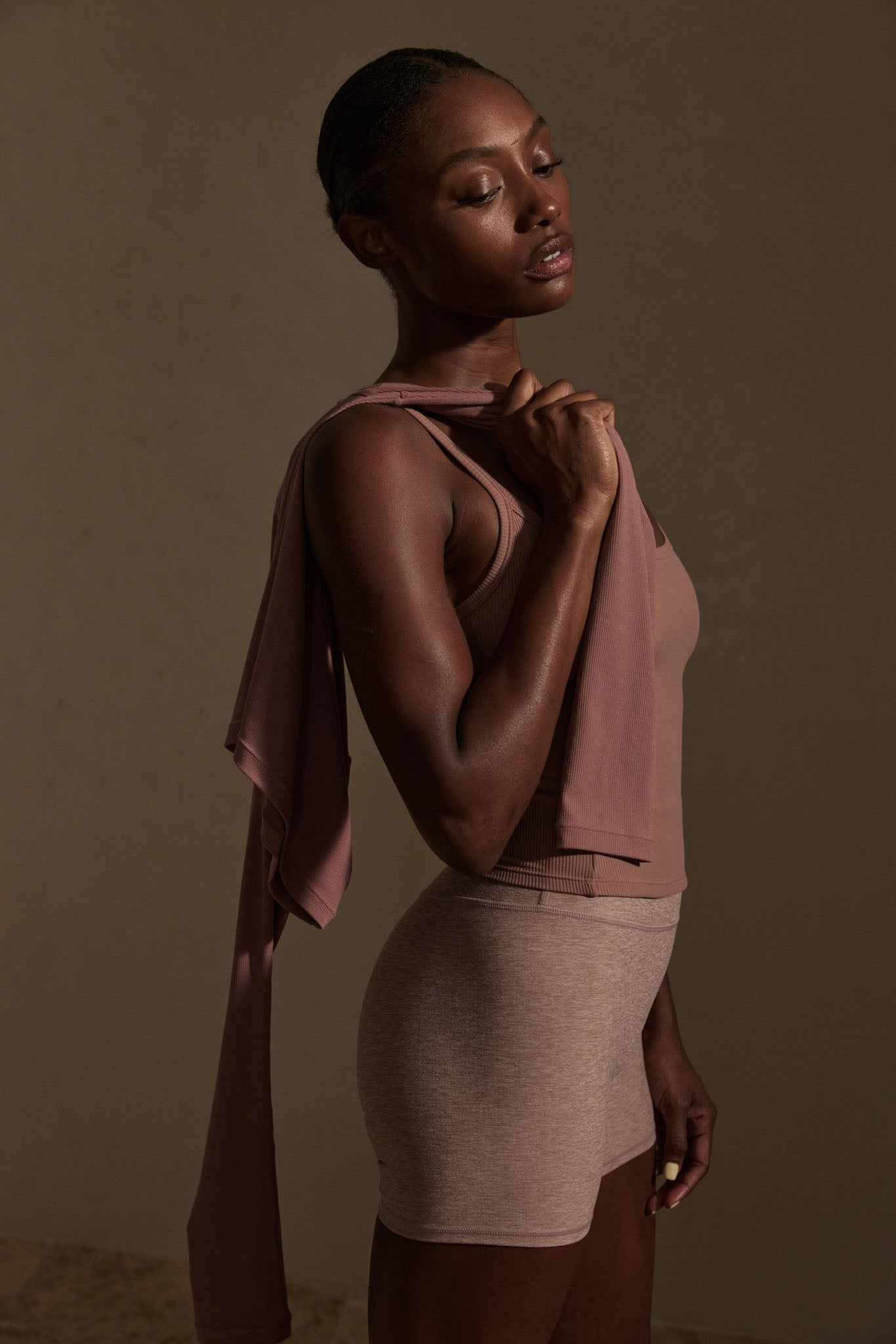 Model wearing heather mauve ribbed tank and Elysian shorts, side profile holding fabric draped over her shoulder.