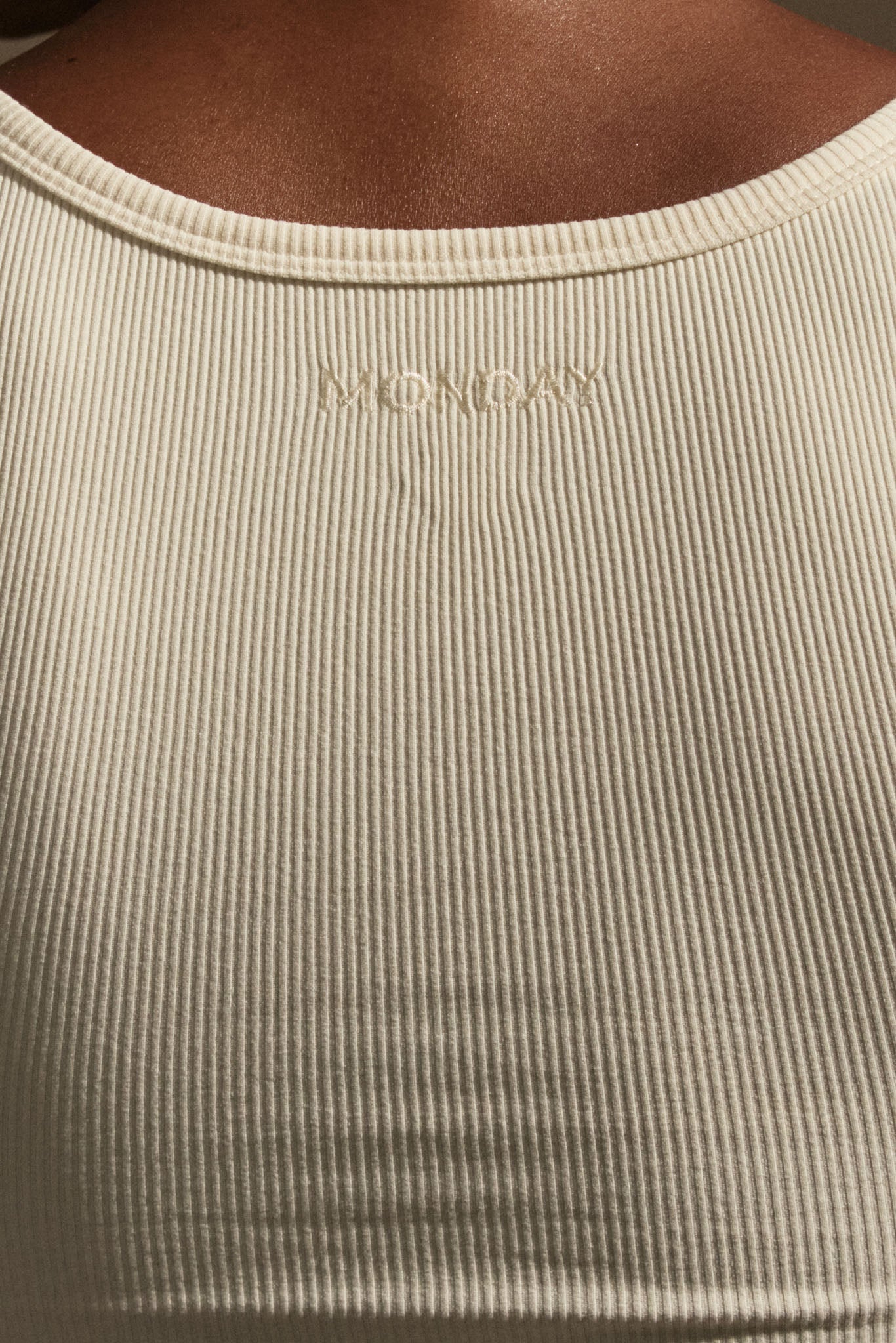 Close-up of ribbed cream tank back with small embroidered 'MONDAY' centered below the neckline.