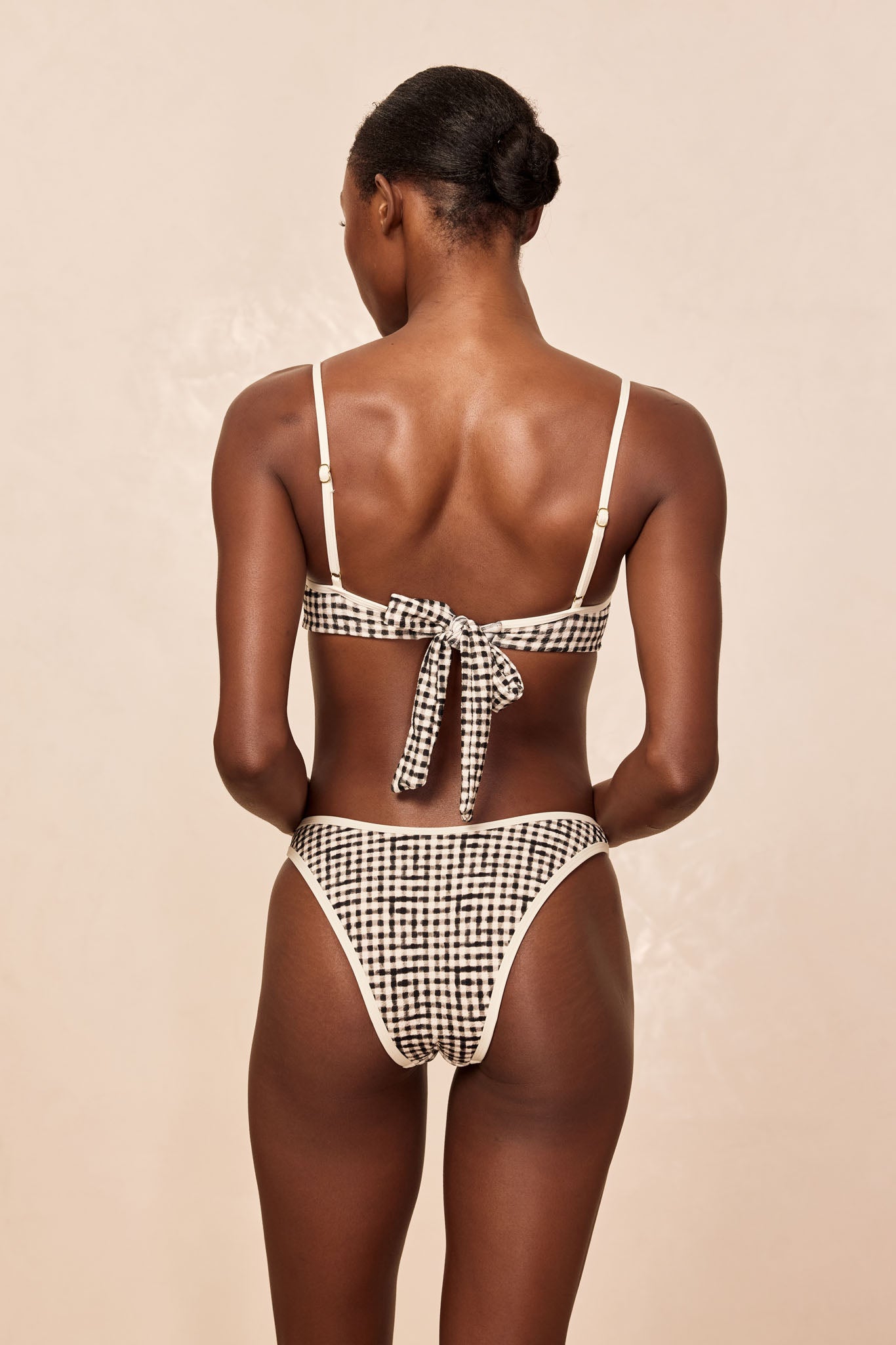 Back view of model wearing black-and-white gingham bikini with tied bow at center back