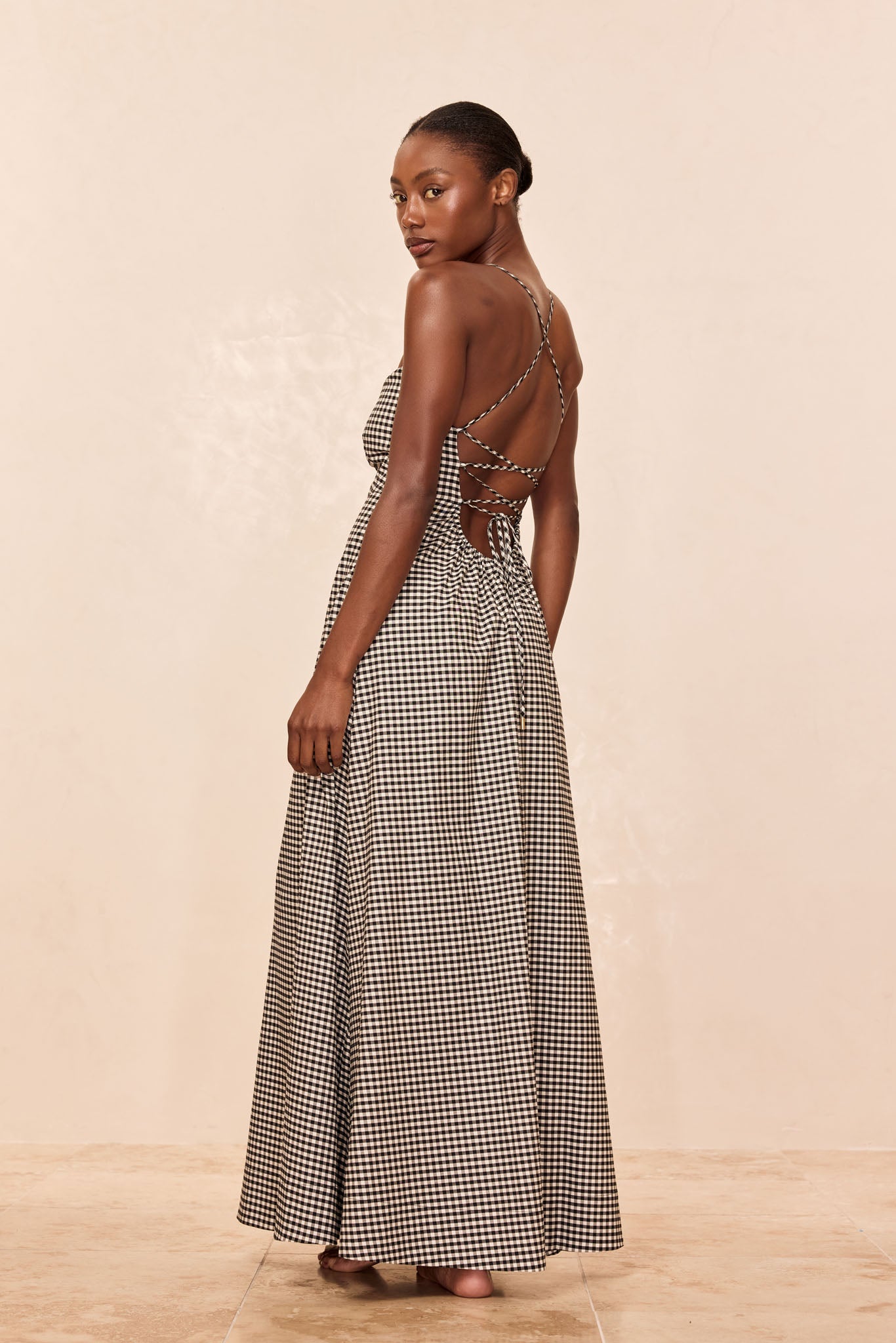 Woman in black-and-white gingham backless maxi dress with crisscross tie straps, shown from a three-quarter back view.