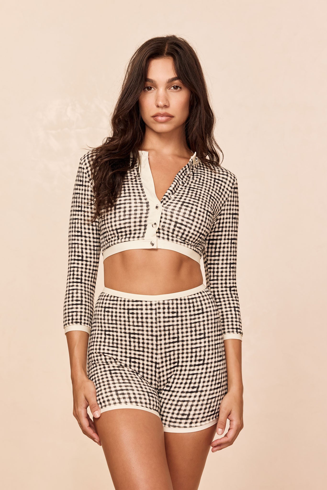 Woman wearing black-and-white gingham cropped button-front cardigan and matching high-waist shorts on a neutral beige background.