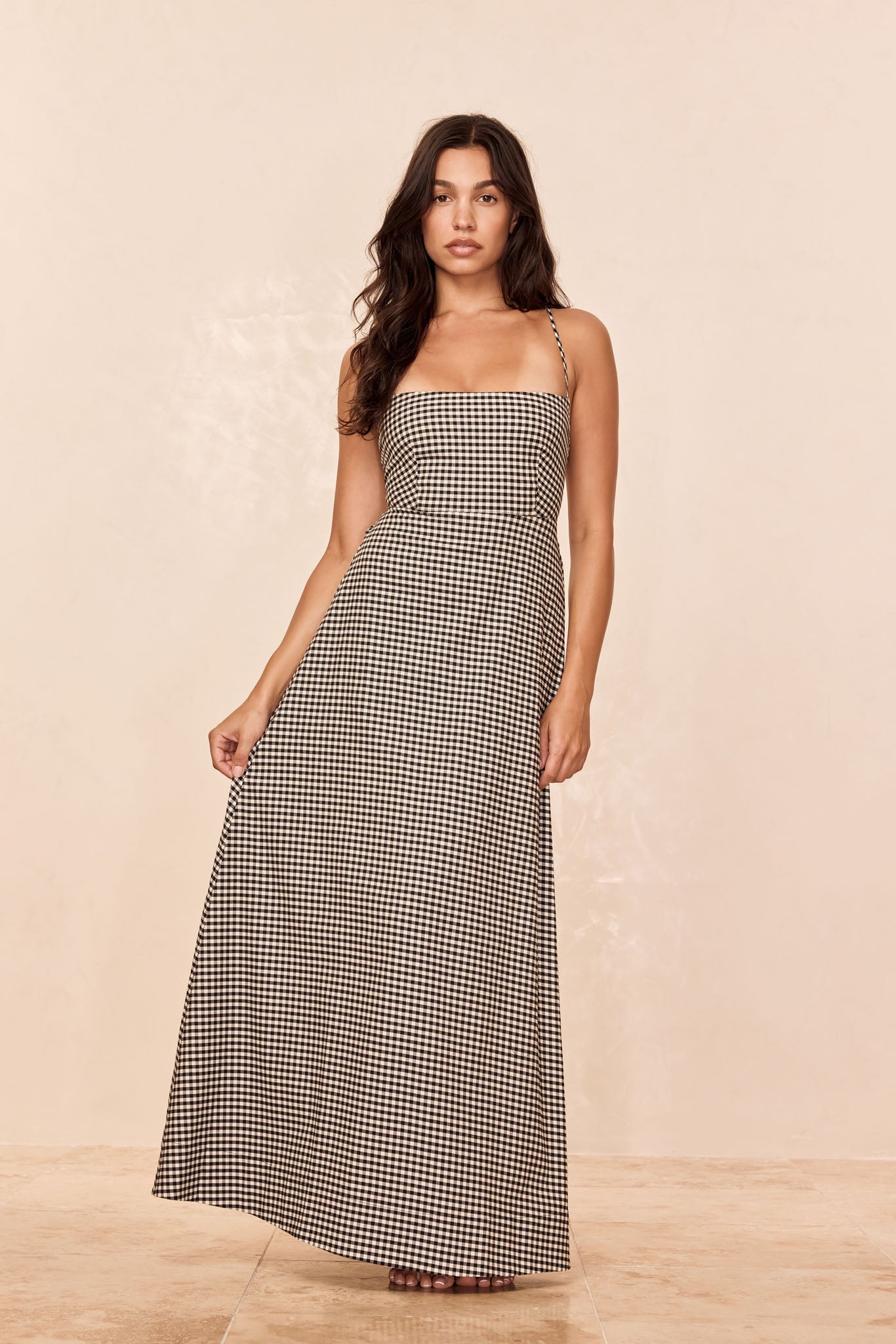 Woman wearing black-and-white gingham strap maxi dress, standing against neutral background, full-length view