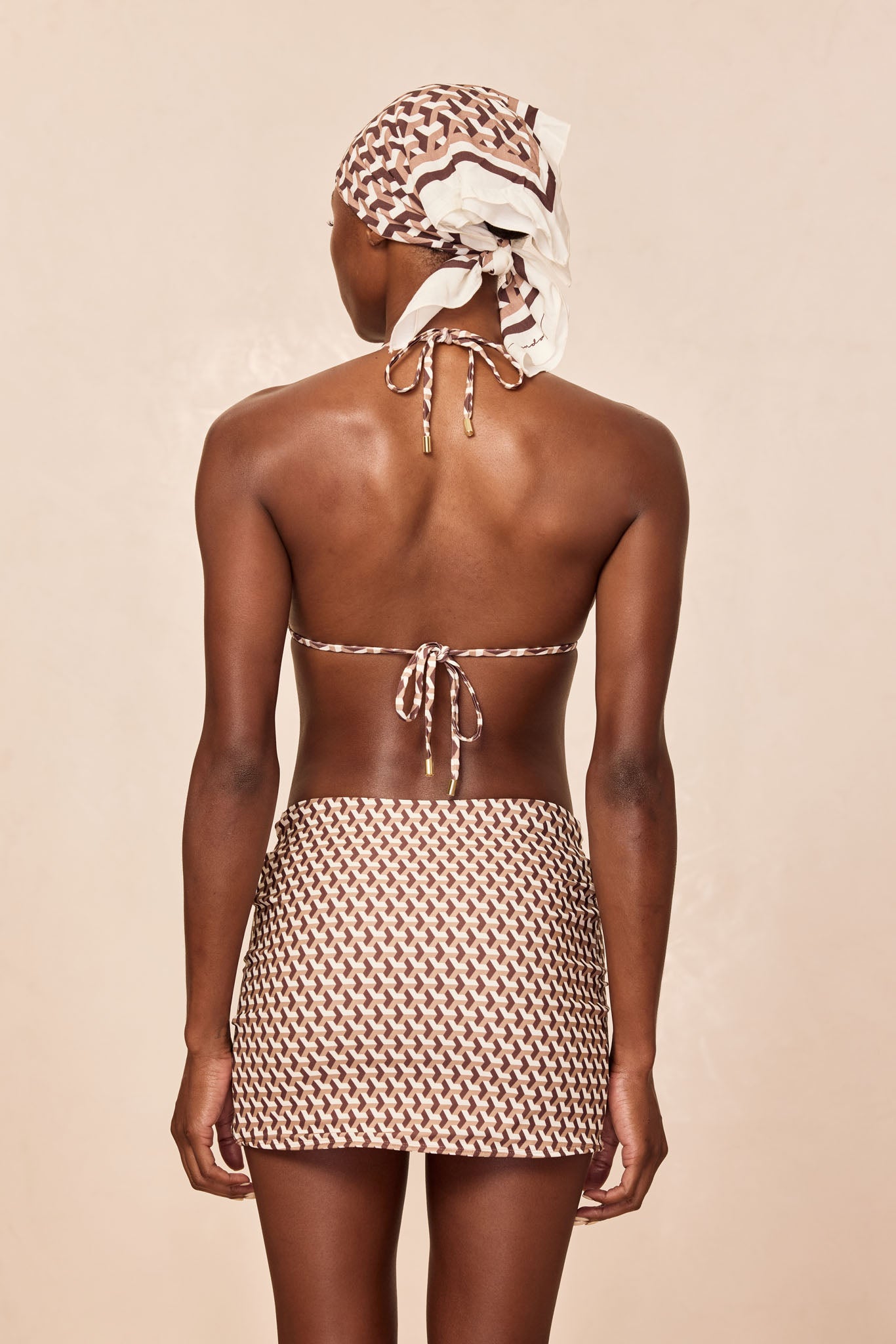 Woman from back wearing patterned headscarf, tied triangle bikini top, and matching mini skirt.