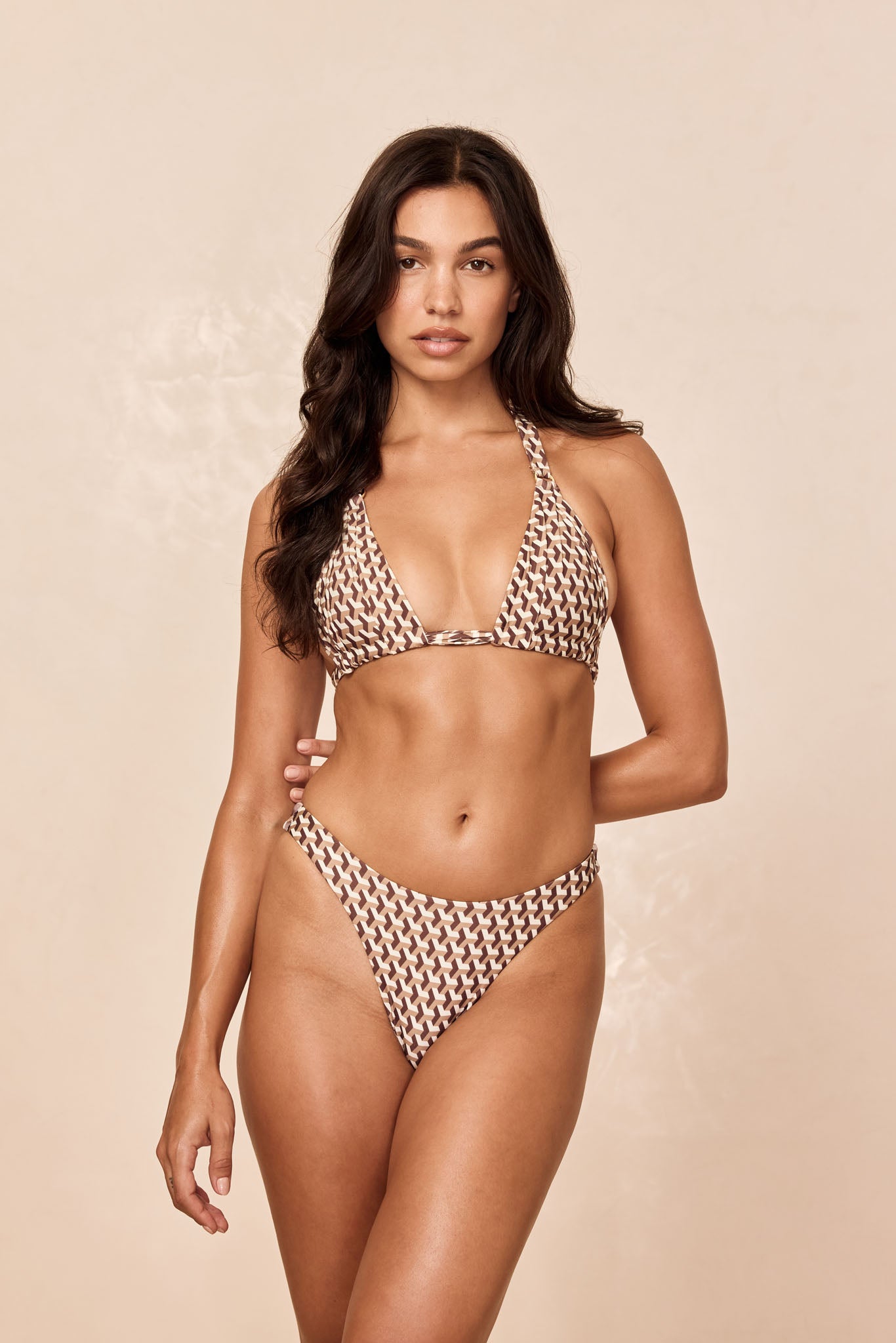 Model wearing brown-and-cream geometric halter bikini, front-facing against a beige background.