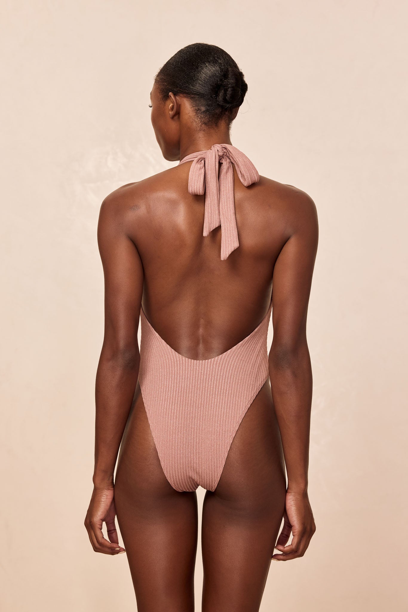 Back view of woman wearing ribbed dusty-pink halter one-piece swimsuit tied at the neck.