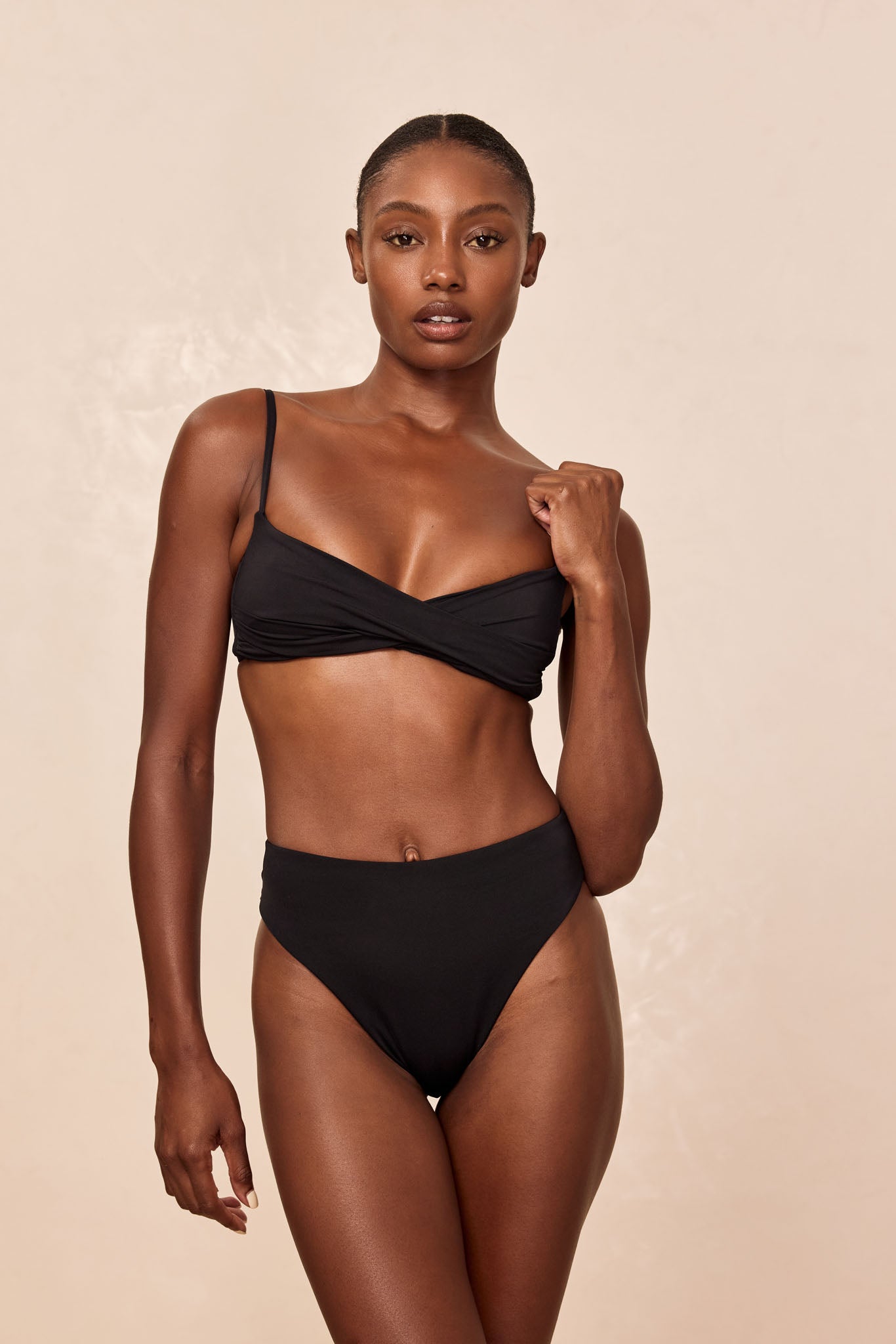 Woman wearing black two-piece swimsuit with twist-front top and high-waist bottoms against neutral background