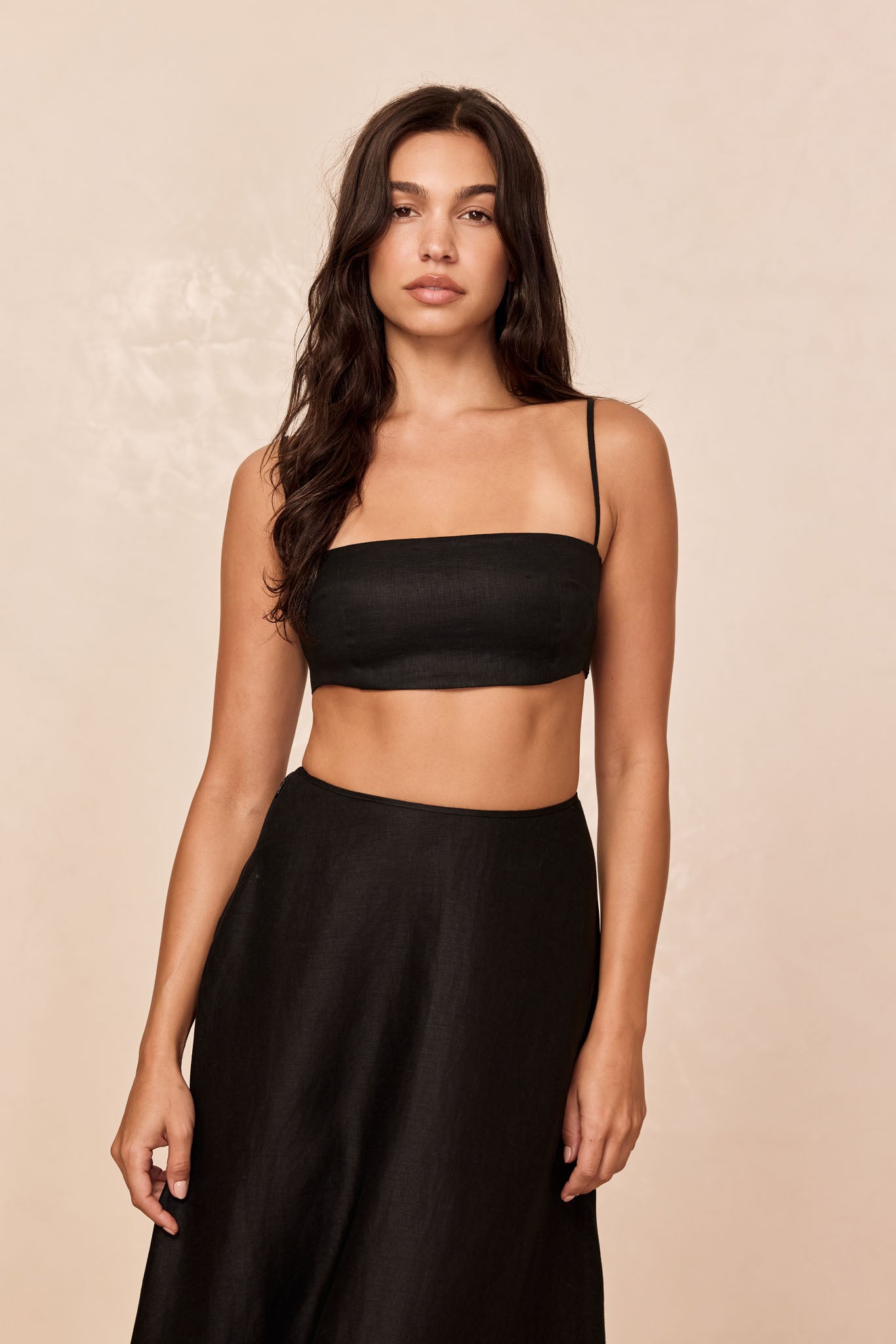 Model wearing black bandeau crop top and high-waist skirt against beige backdrop