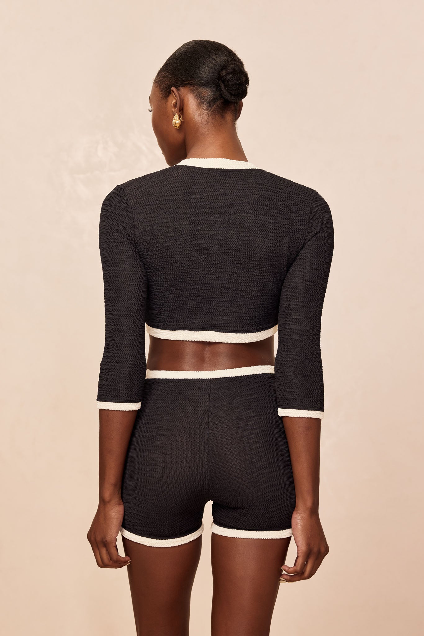 Back view of model wearing black textured cropped top and matching high-waist shorts with white trim.