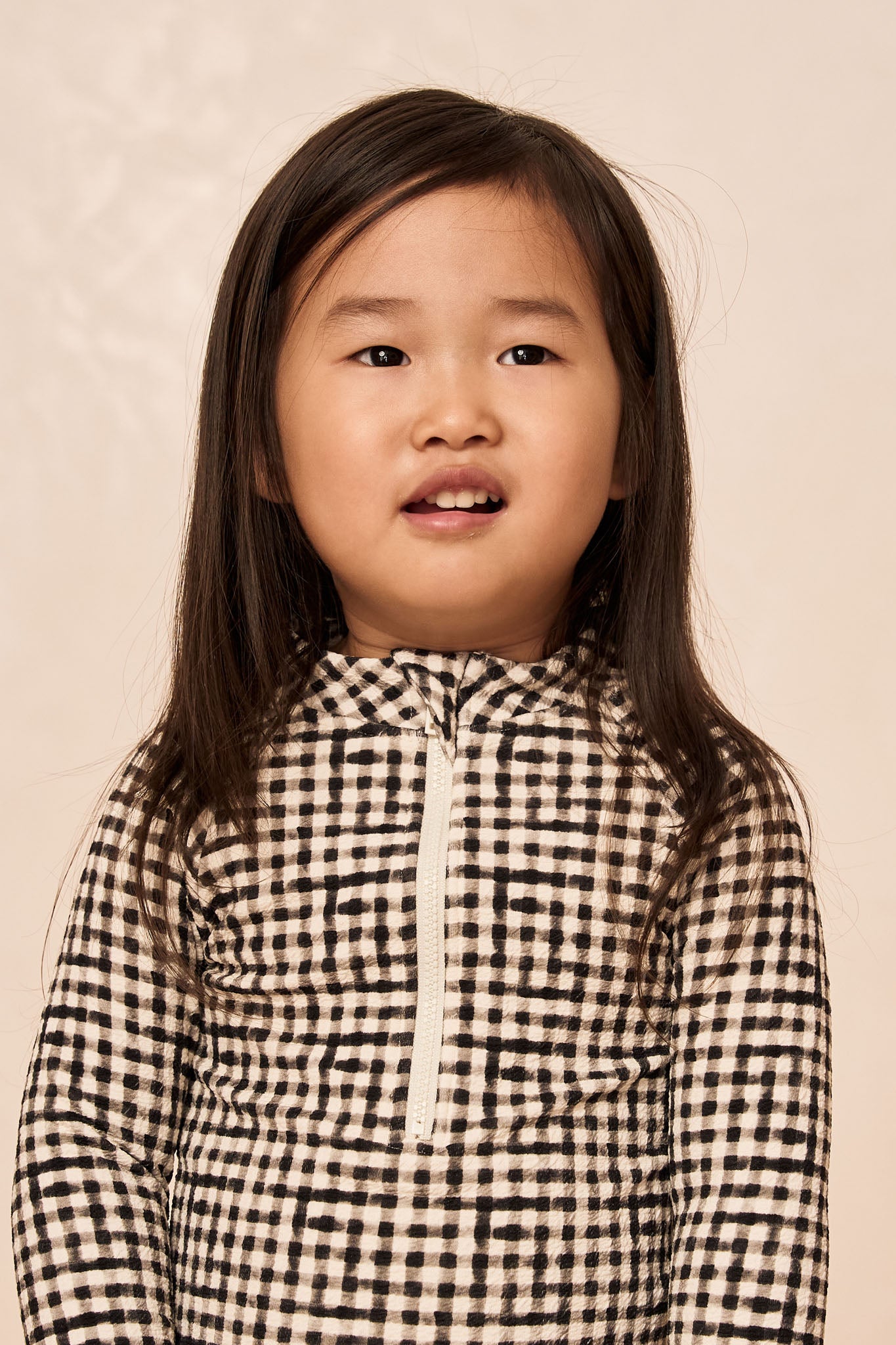 Girl with long dark hair wearing a black-and-white checkered zip-up top, looking slightly upward.