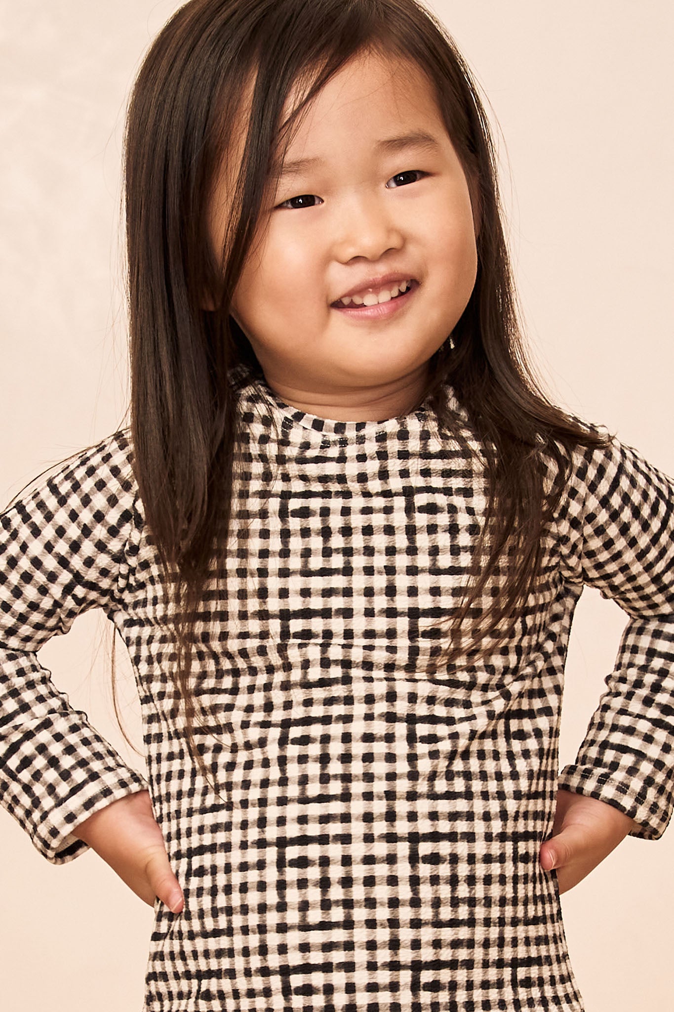 Smiling child wearing black-and-white gingham dress, hands on hips
