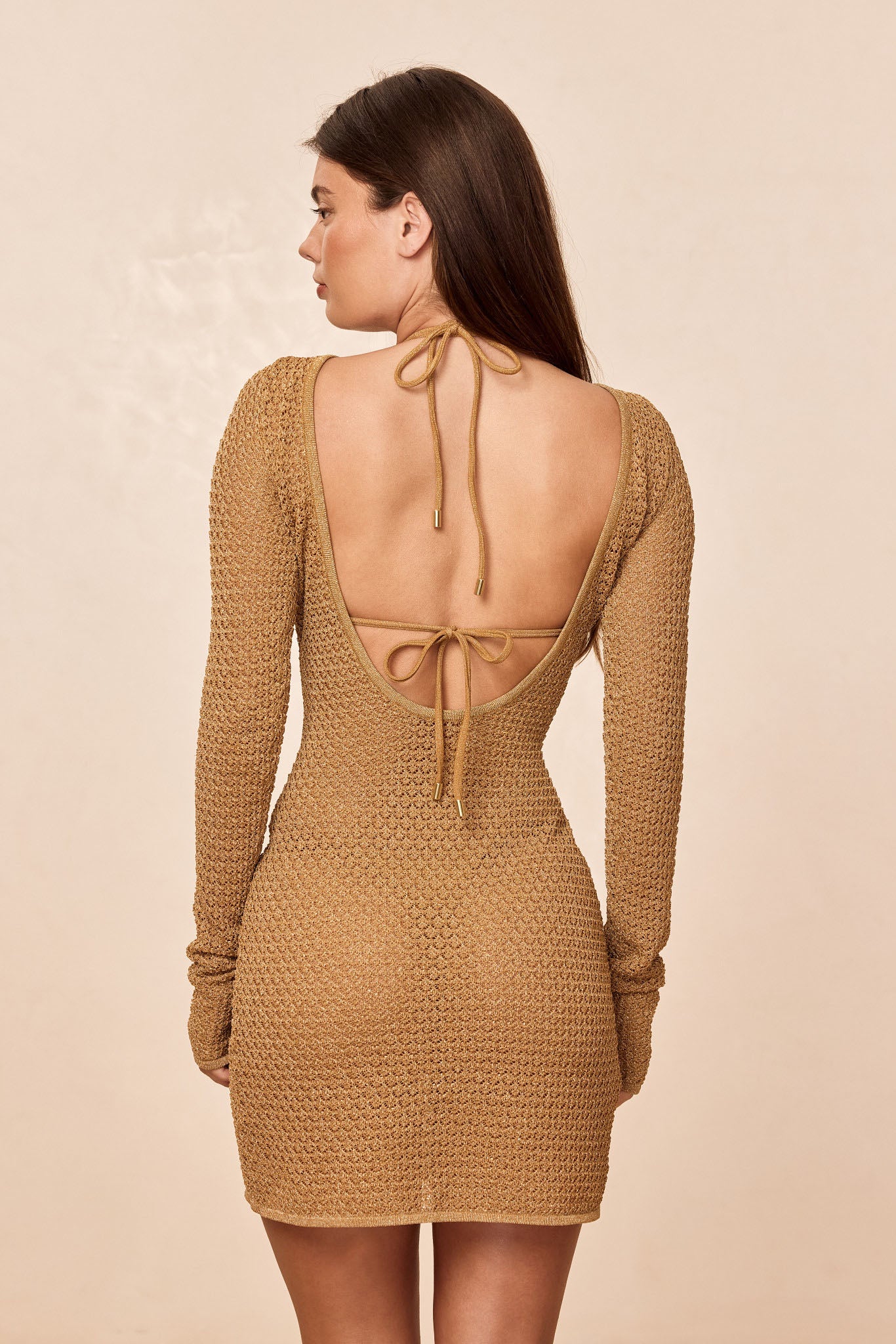 Rear view of Bodrum Mini Dress in antique gold lurex crochet showing scooped open back with tied straps on beige background