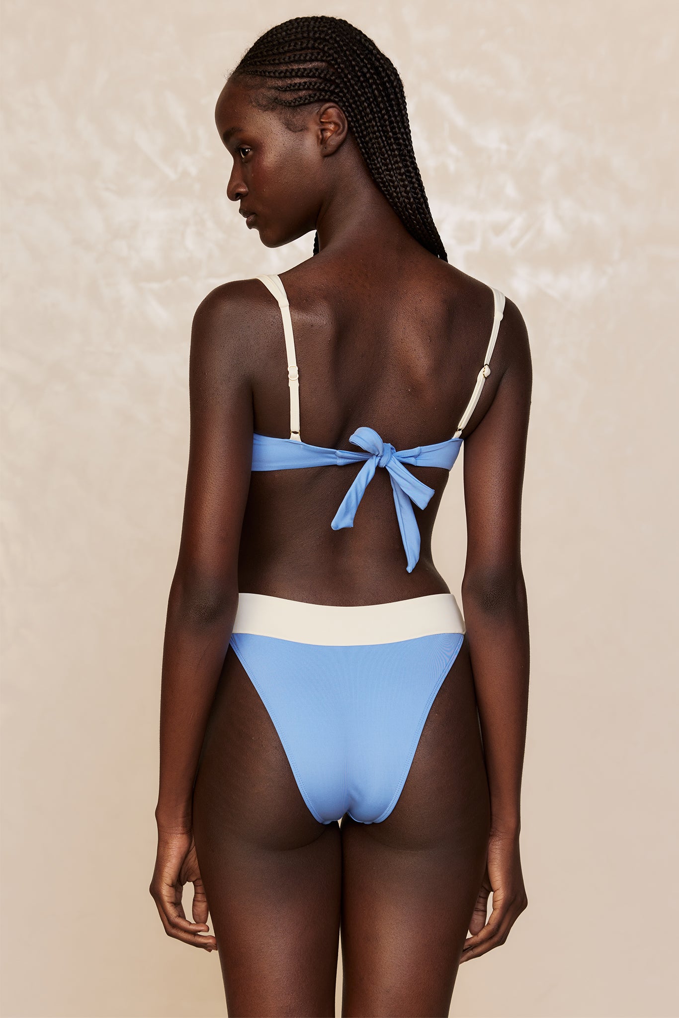 Back view of a model wearing a light-blue bikini with cream straps and a tied bow at the back.