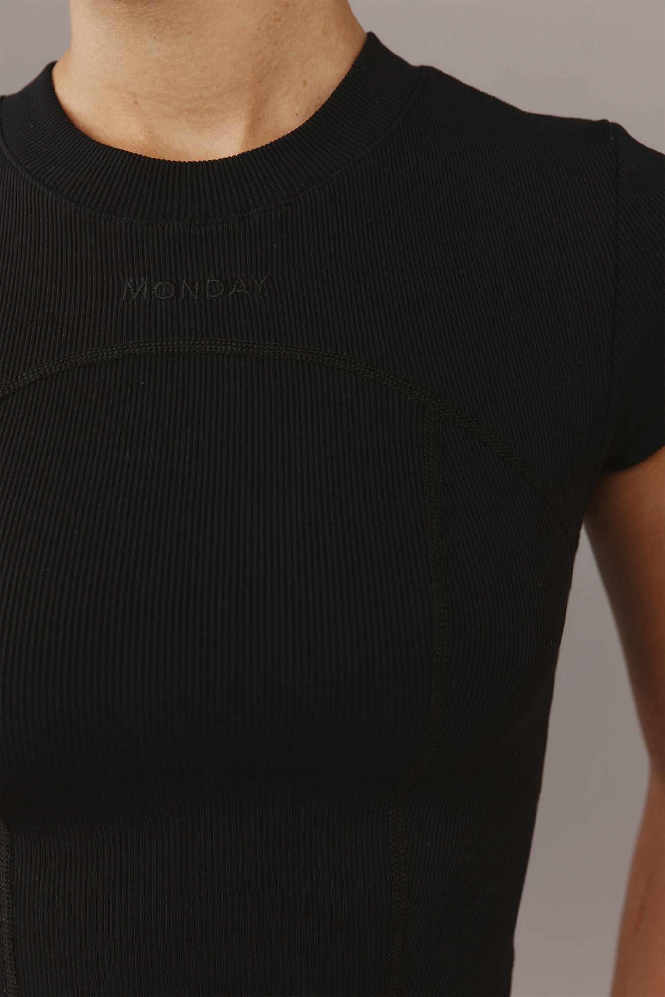 Black ribbed short-sleeve top with stitched "MONDAY" logo at upper chest, crew neckline and curved seam details.