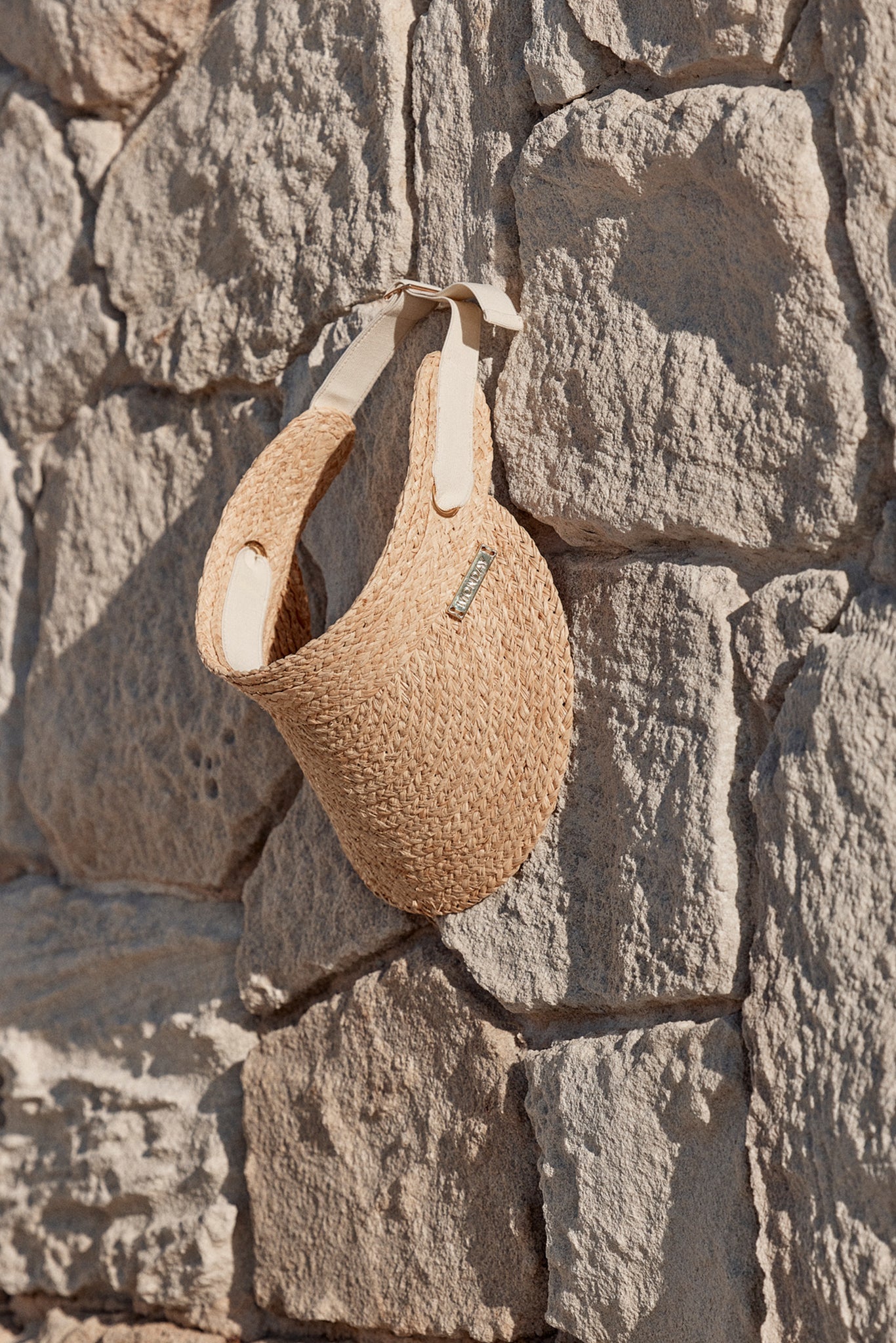 Woven straw visor hanging on a sunlit stone wall.