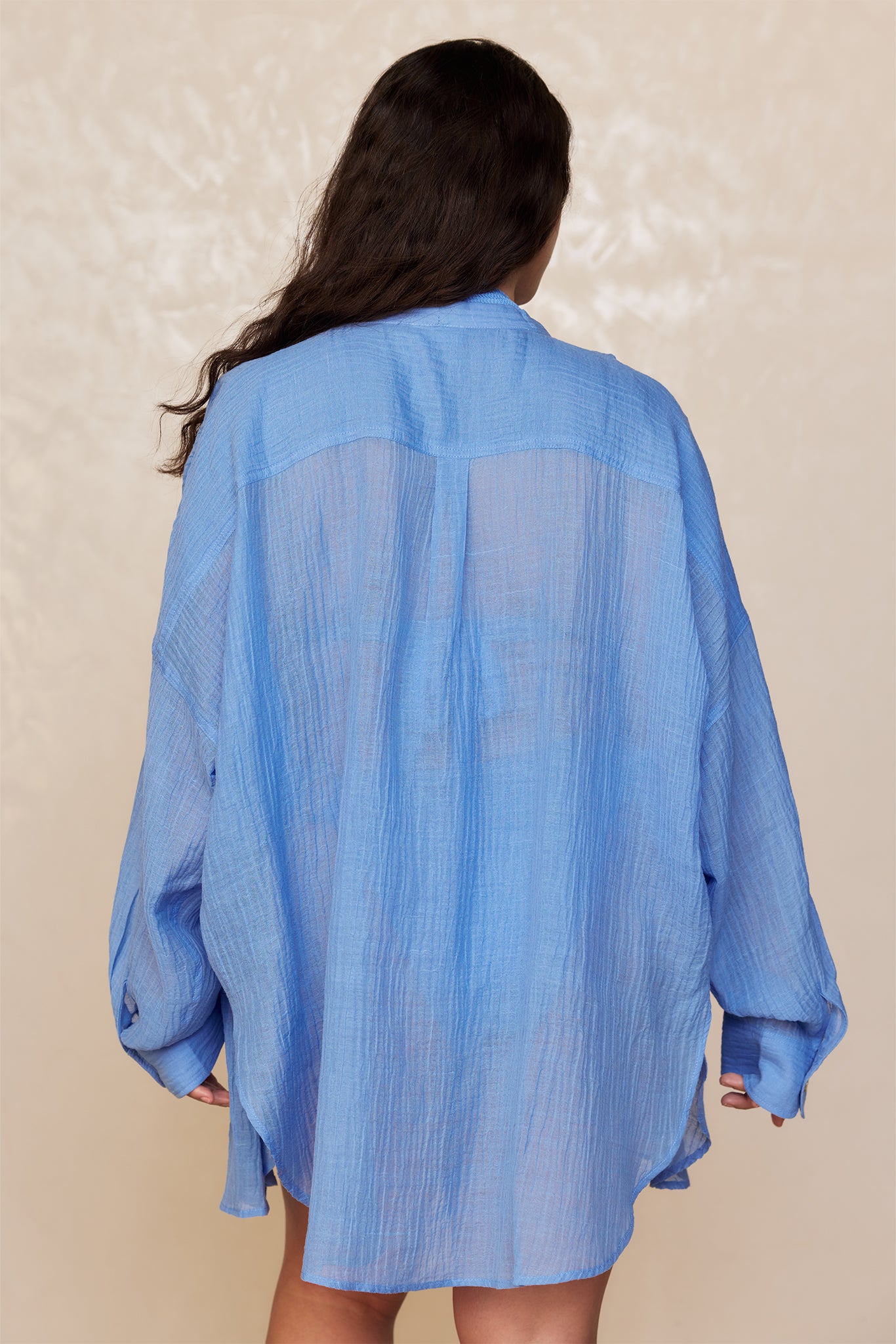 Person seen from behind wearing an oversized sheer light-blue shirt with loose sleeves, hair down