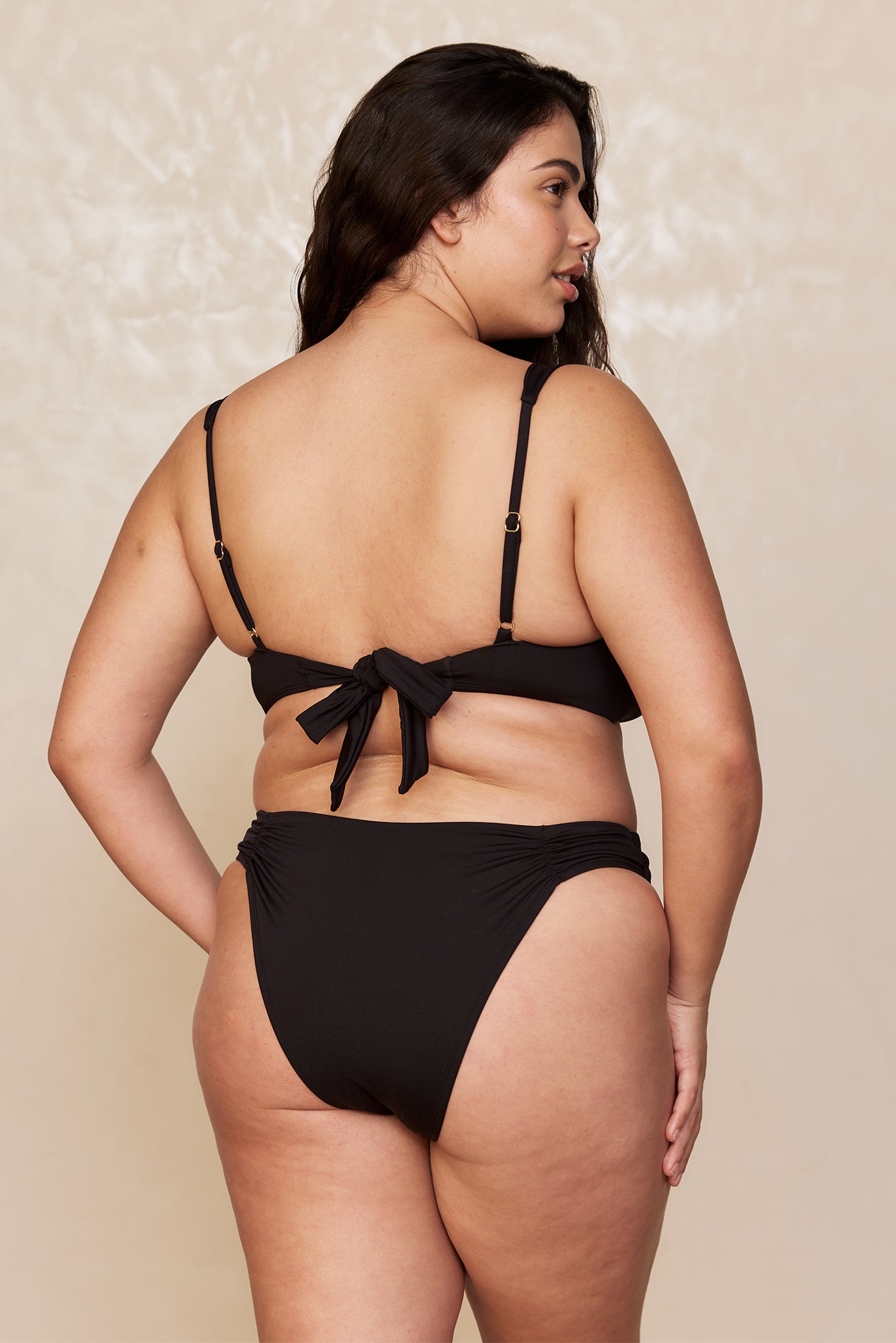 Back view of a plus-size model wearing a black tie-back bikini with high-cut bottoms.