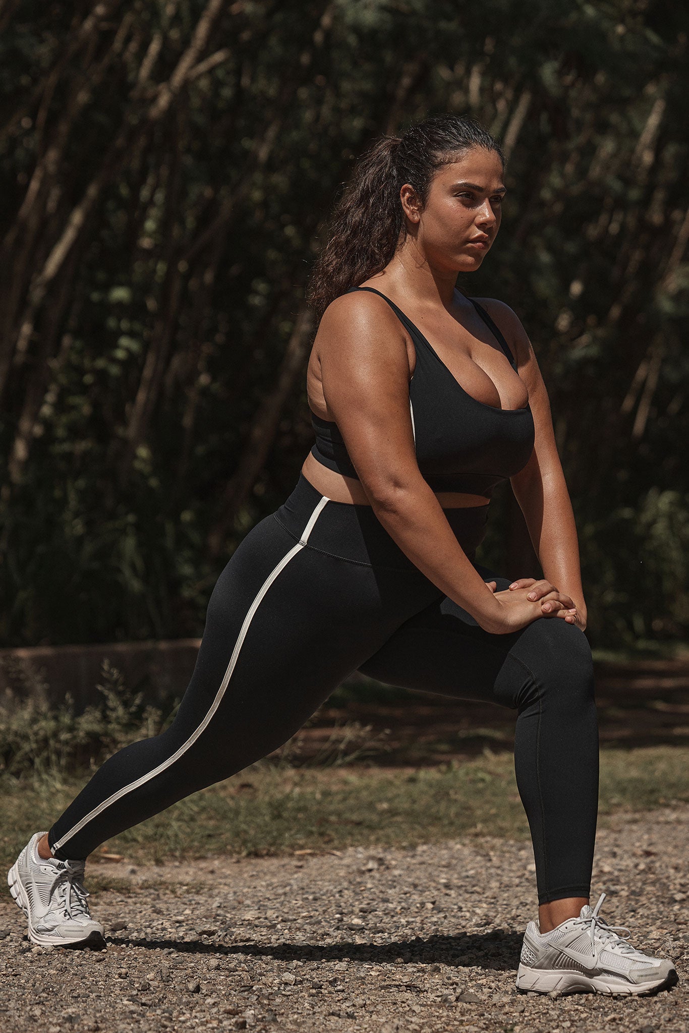 Woman in black sports bra and leggings doing a forward lunge outdoors on gravel path