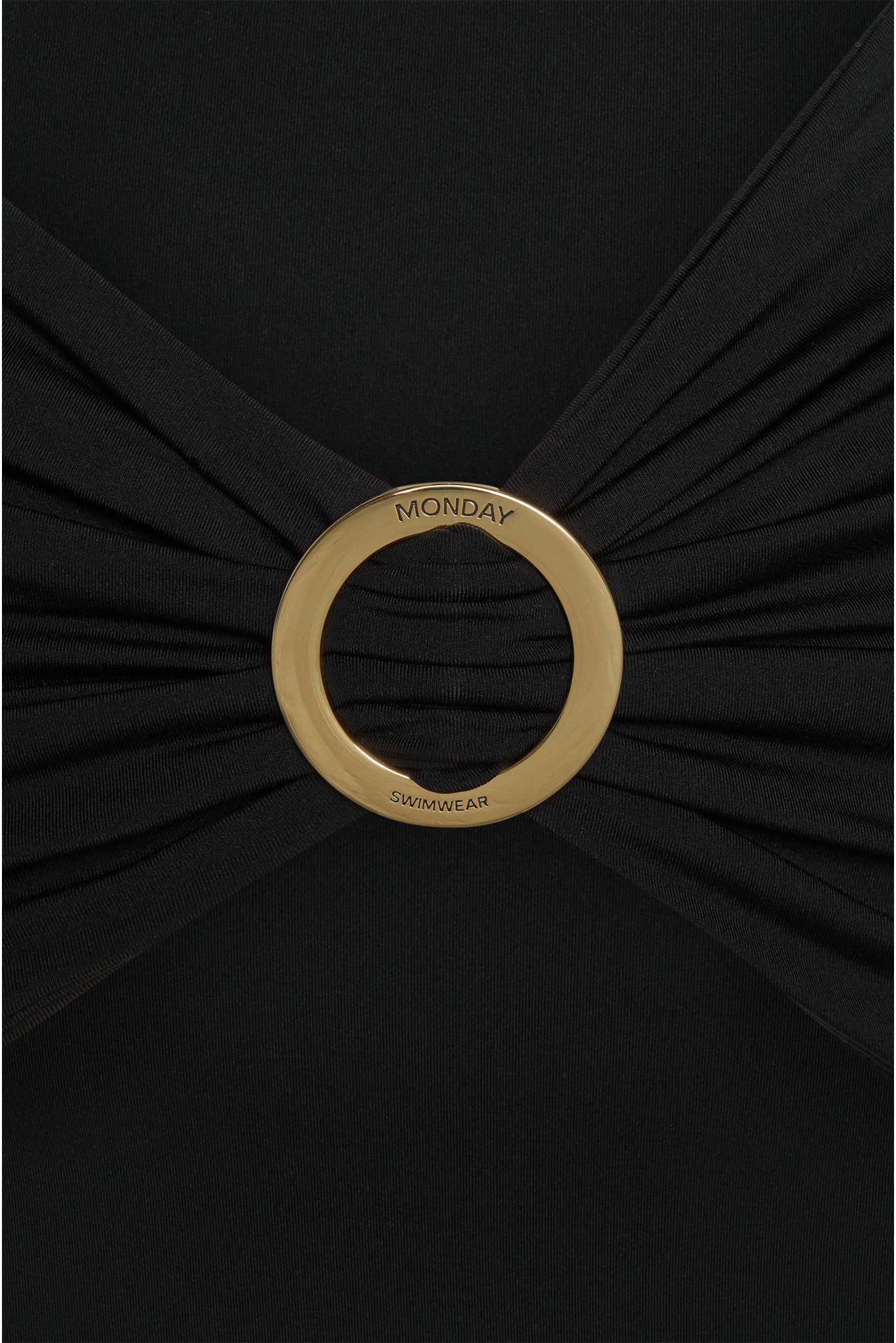 Gold circular buckle engraved 'MONDAY' and 'SWIMWEAR' on a black ruched swimsuit