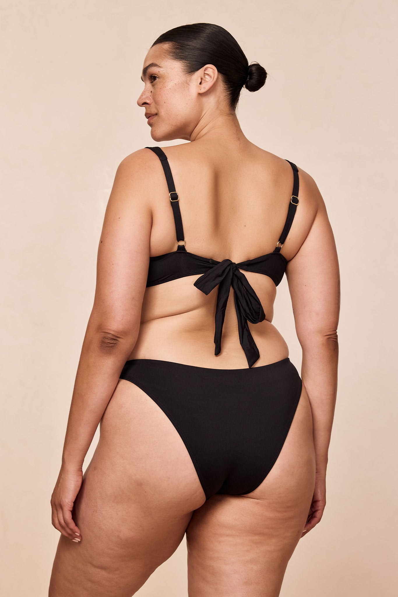 Back view of model wearing a black bikini with tied bow at the back and high-cut bottoms