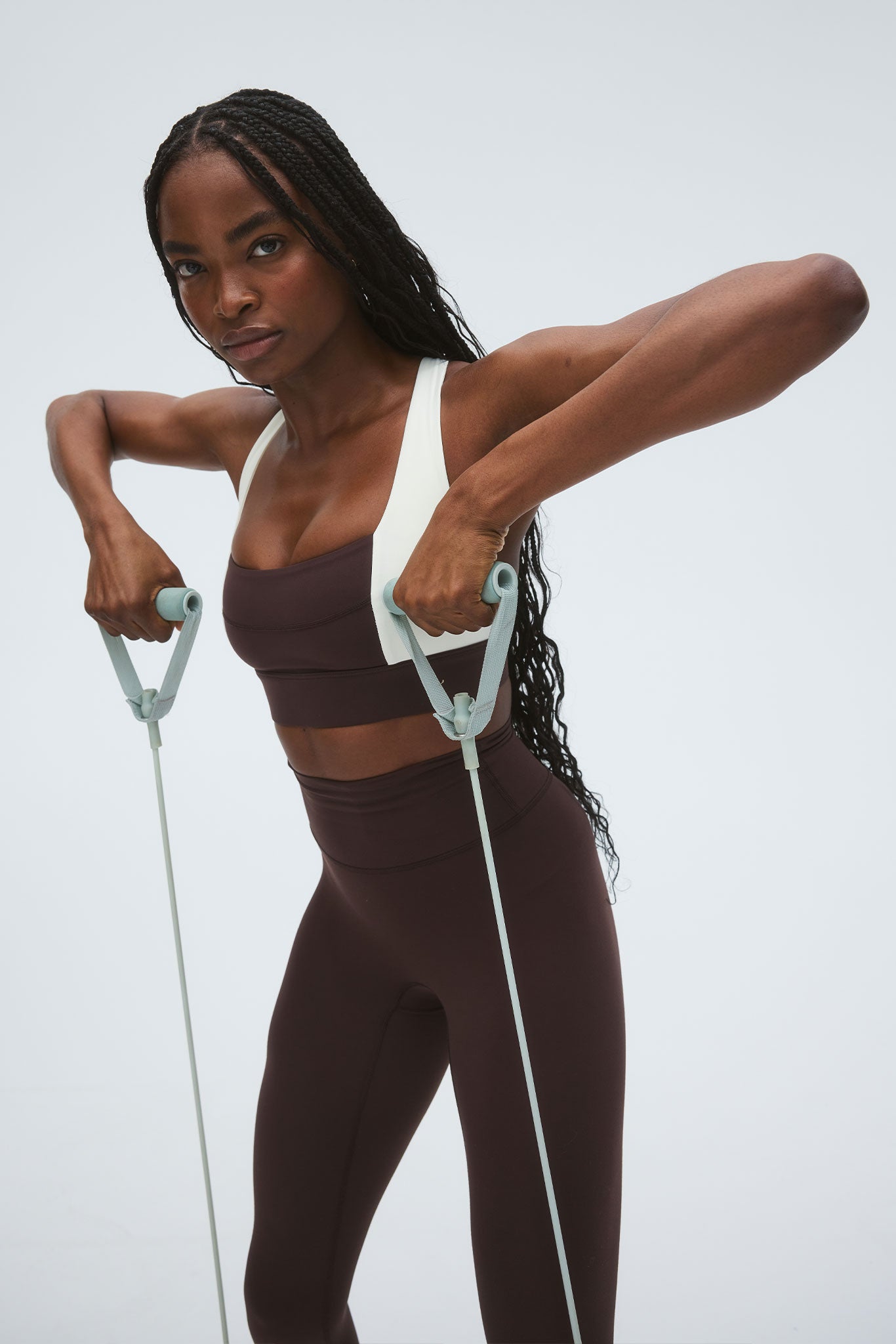 Person performing an upright-row with a mint-green resistance band, wearing dark brown sports bra and high-waist leggings.