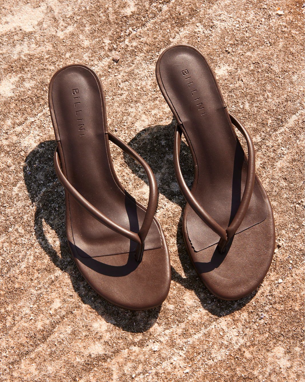 Brown BILLINI thong sandals on sandy ground, overhead view