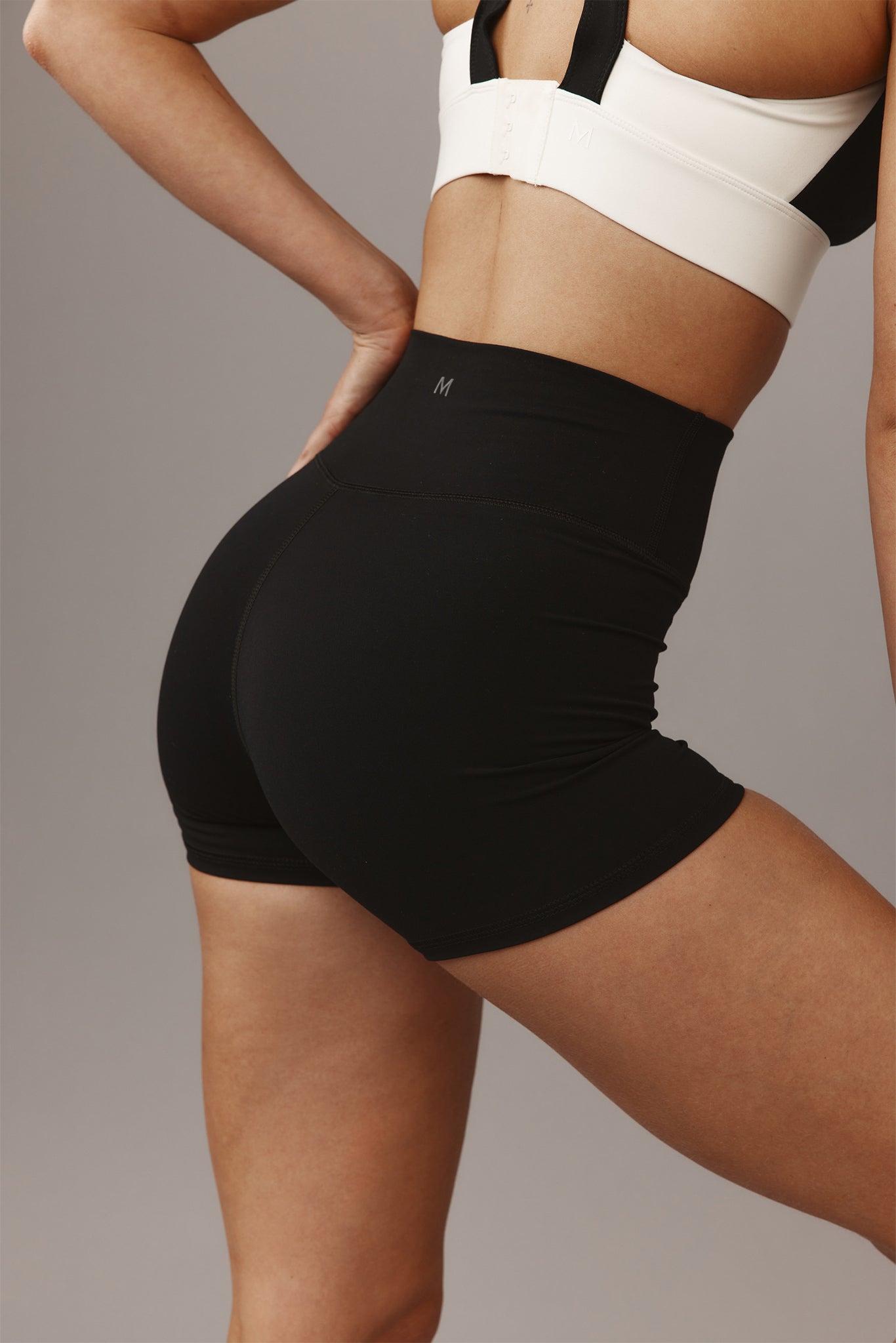 Rear view of person wearing high‑waist black athletic shorts and a white sports bra; visible 'M' logo on waistband