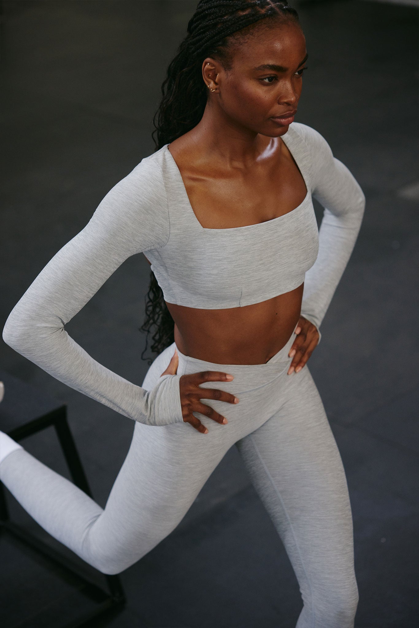 Athletic woman in light-gray long-sleeve cropped top and high-waist leggings doing a lunge with hands on hips.