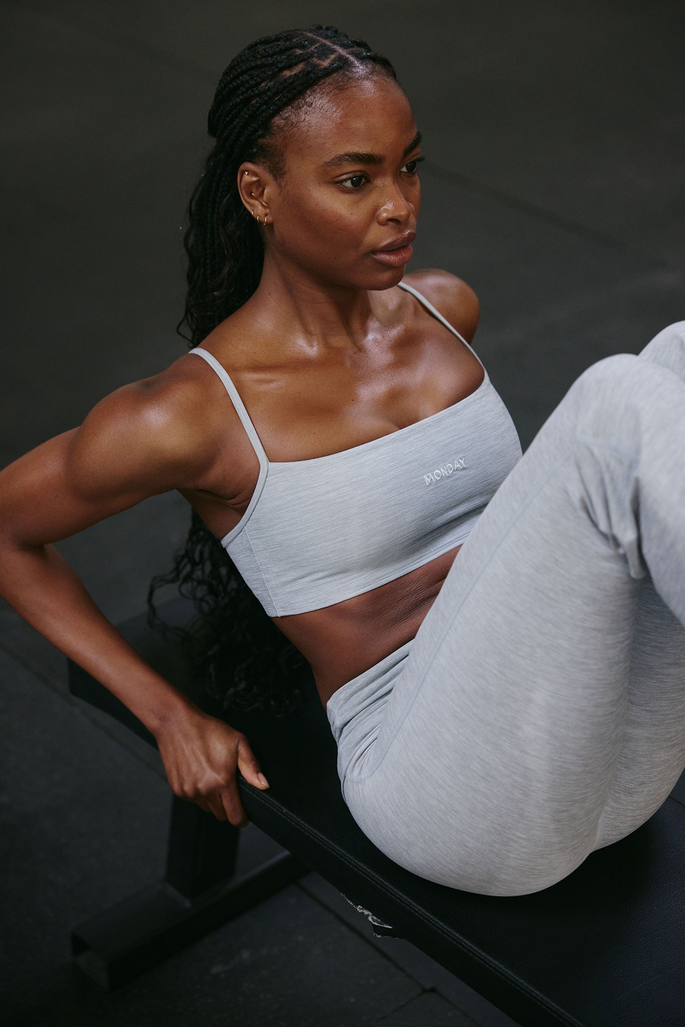 Woman doing crunches on a workout bench, wearing light gray sports bra labeled MONDAY and matching leggings.
