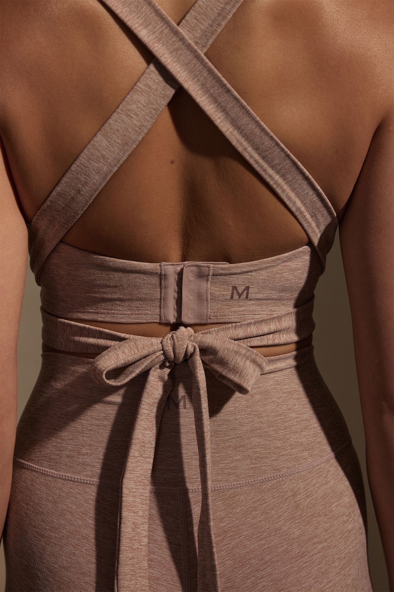 Back view of person wearing mauve cross-strap sports bra and tied waist band showing 'M' logos.