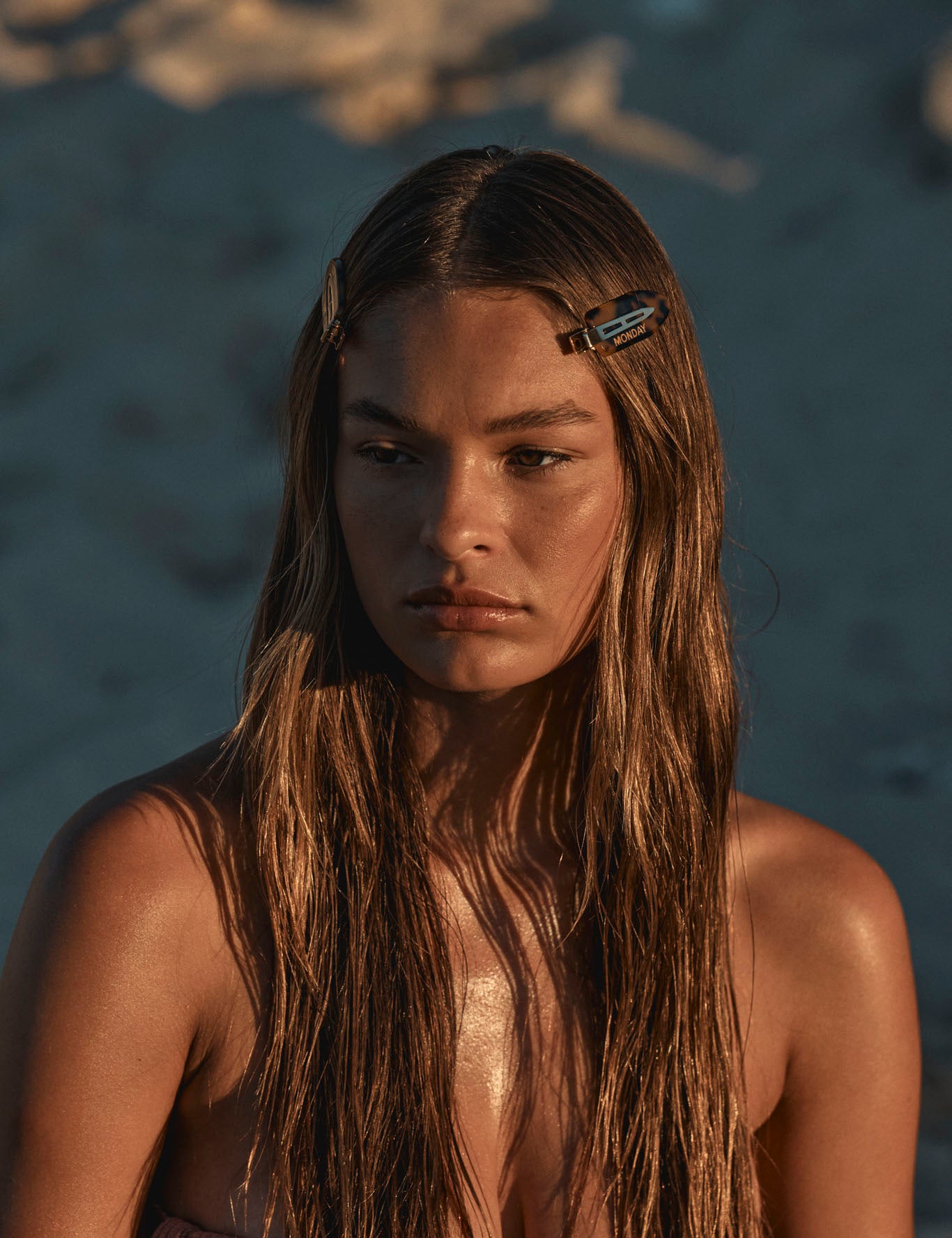 Young woman with long wet hair and two tortoiseshell clips (one reads MONDAY), gazing down in warm sunset light.
