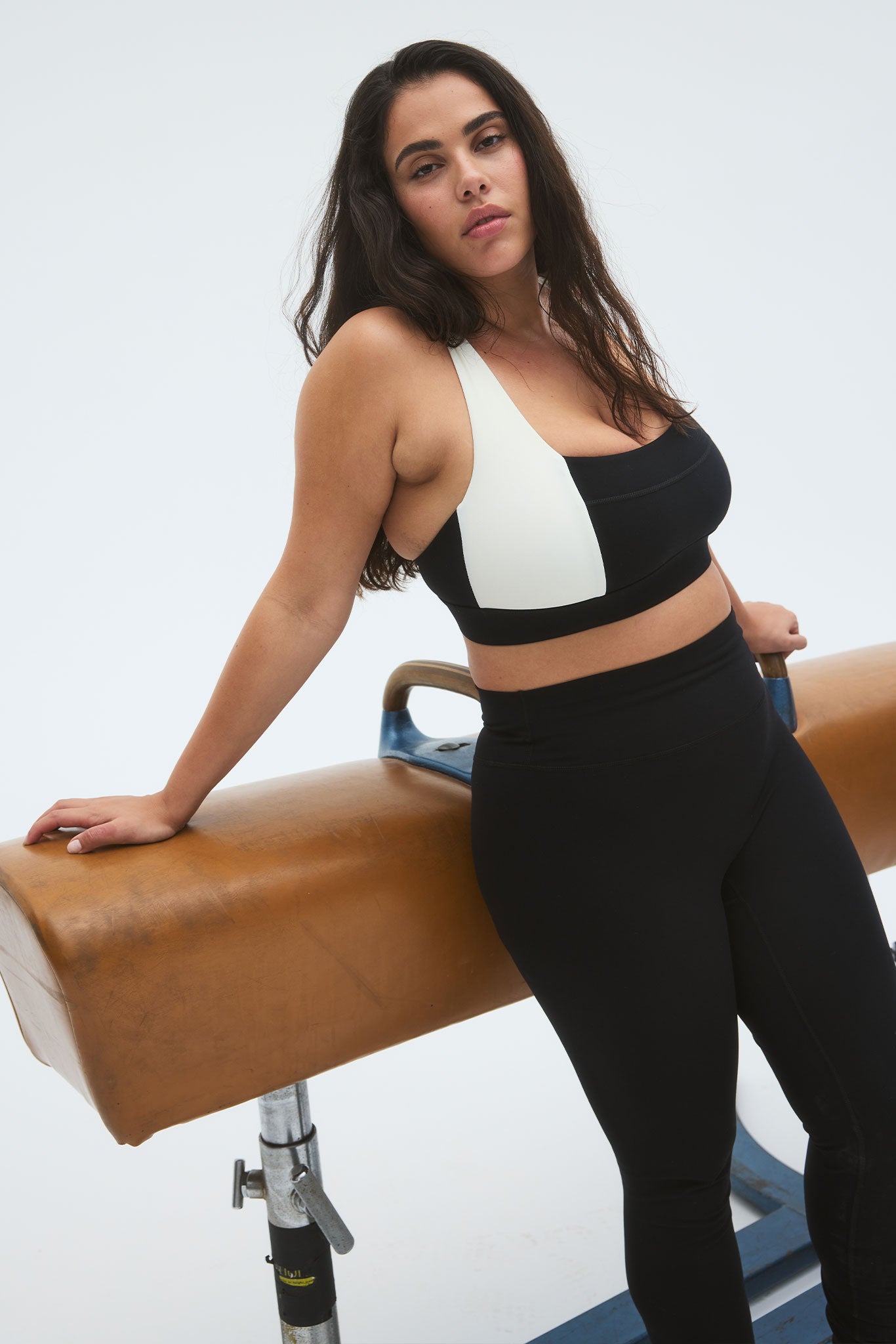 Person wearing a black-and-white sports bra and black leggings leaning on a leather gym pommel horse