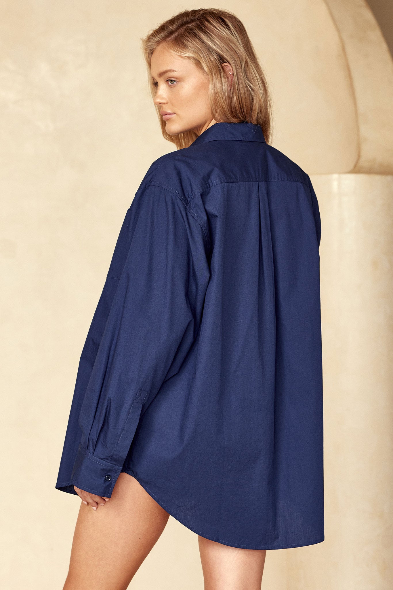 Model wearing oversized navy blue button-down shirt, back view as she looks over her left shoulder.
