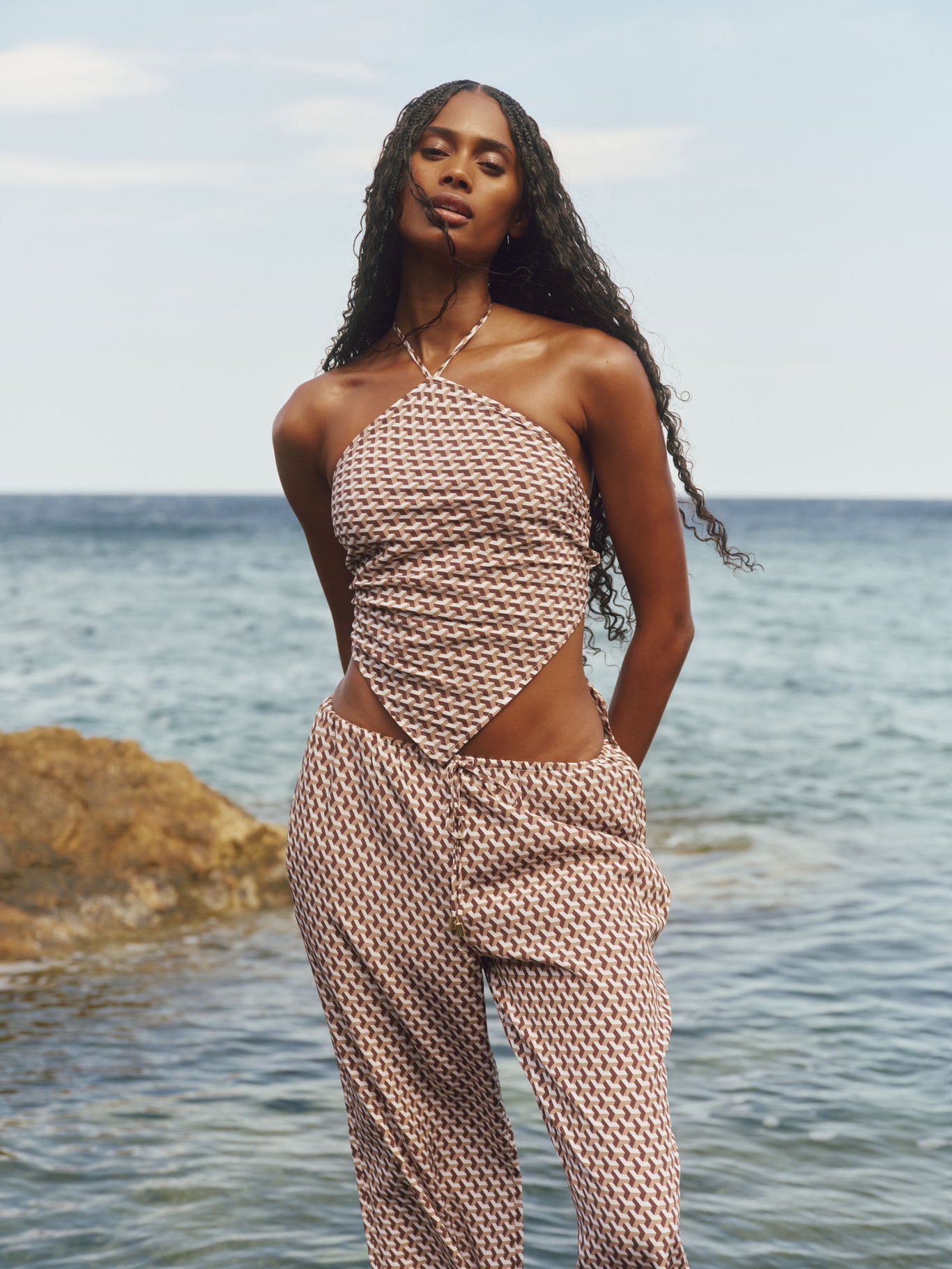 Front view of Prato Top in Husk Geo Silk, brown and cream geometric halter crop on model at ocean