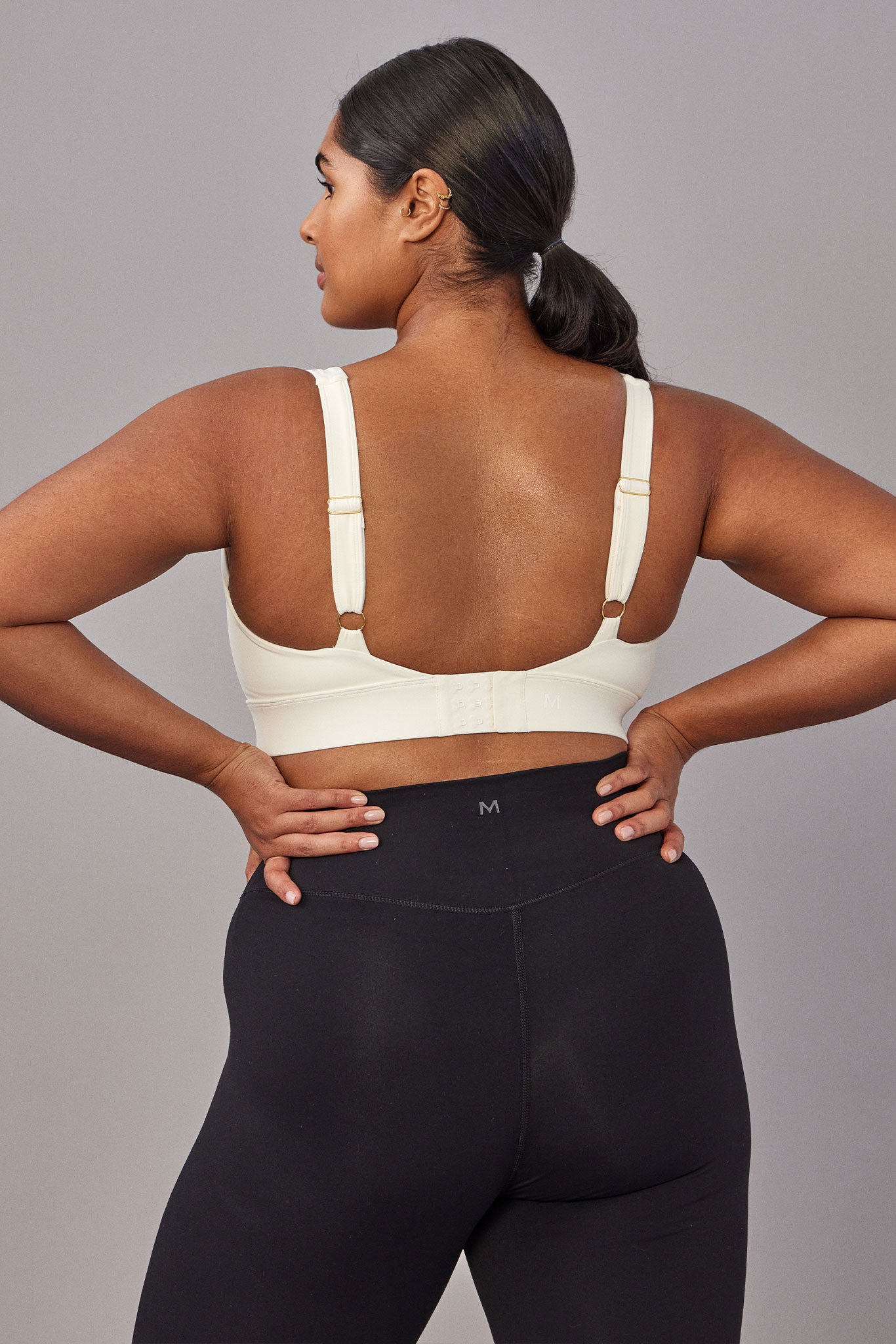 Back view of person wearing cream bra and black leggings with M logo on waistband