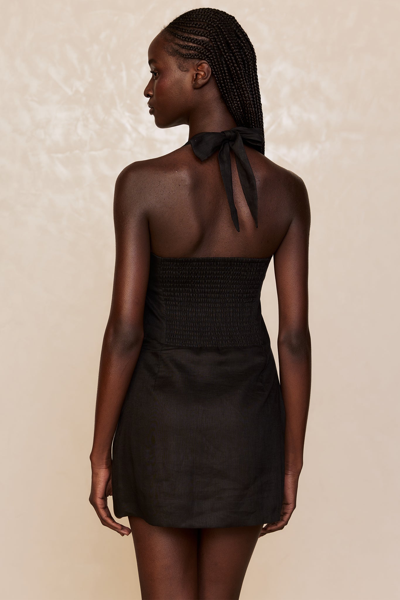 Model wearing black halter mini dress with smocked back, shown from rear