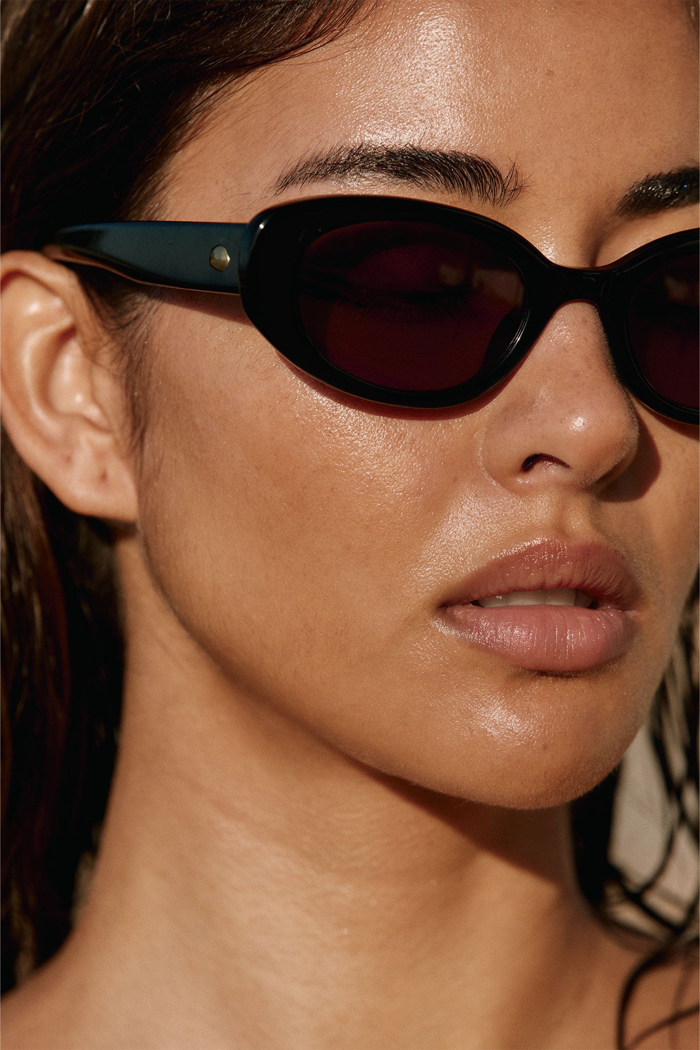 Close-up of a woman’s lower face wearing black cat‑eye sunglasses, sunlit skin and slightly parted lips.