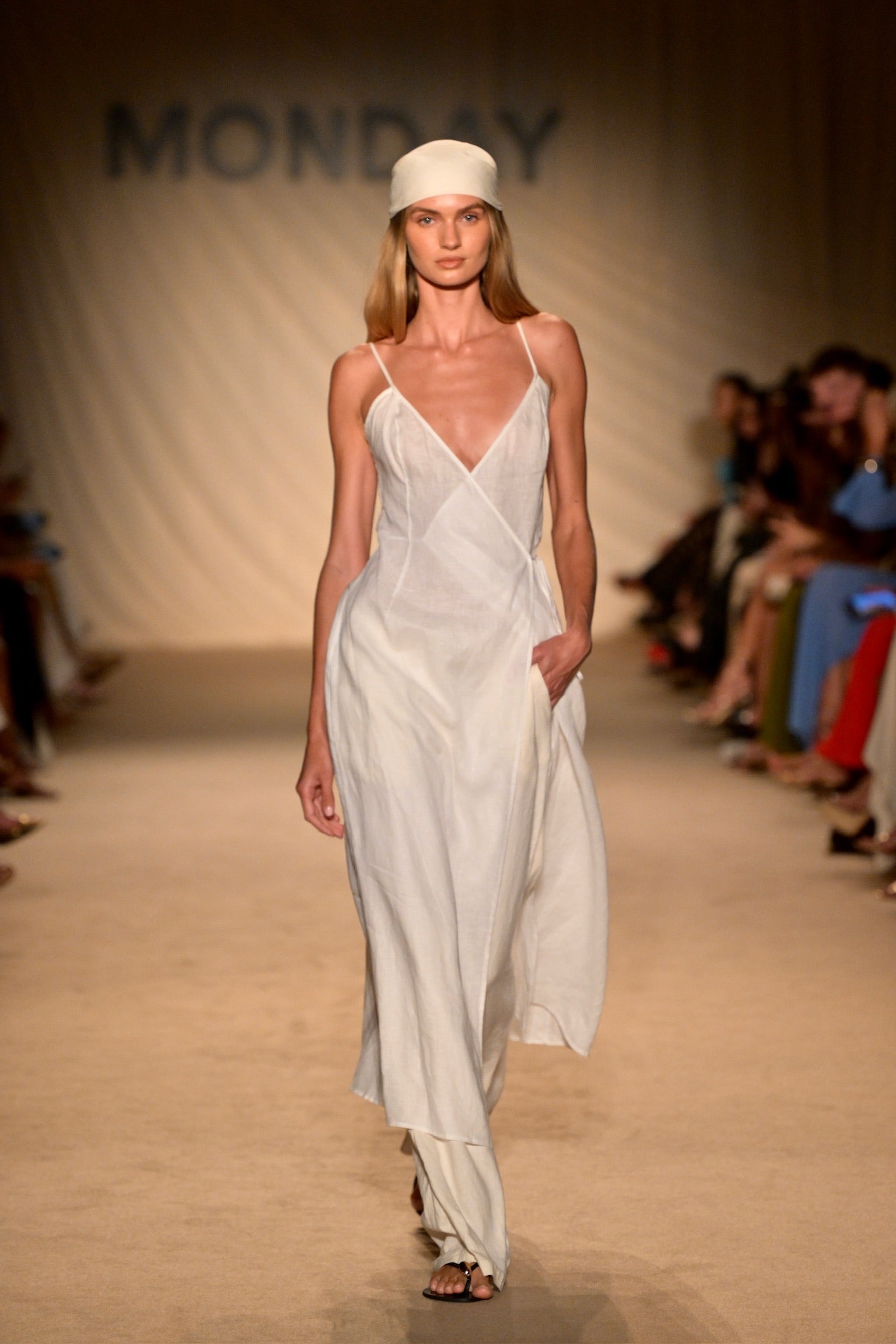 Model walking runway in a flowing white slip dress and headscarf, with 'MONDAY' displayed on the backdrop.