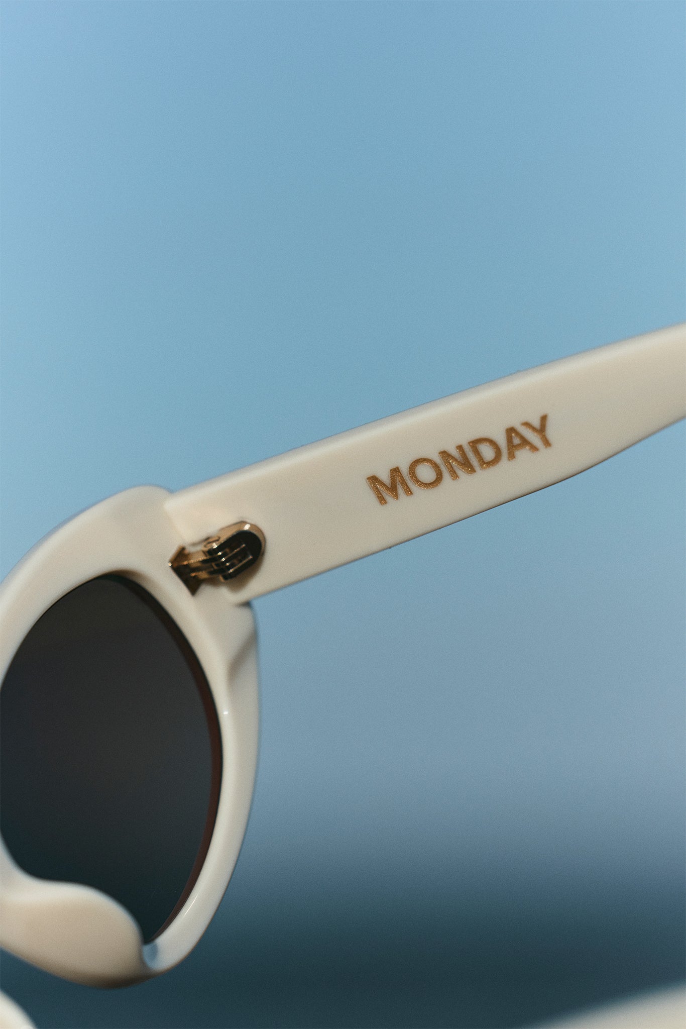 White sunglasses arm with gold MONDAY lettering and hinge against a blue background