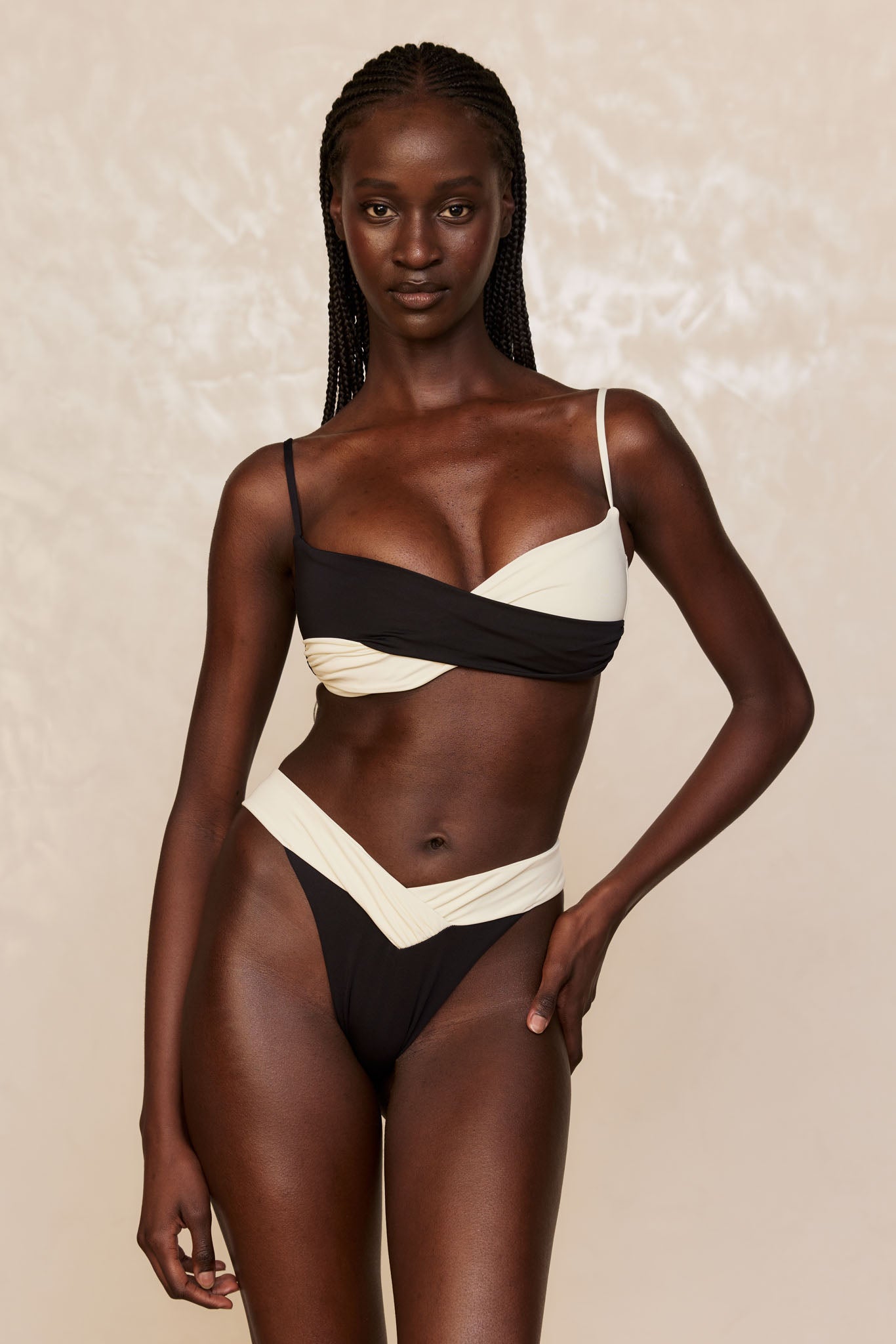 Black-and-cream wrap bikini with high-cut bottoms on a model standing against a neutral backdrop, right hand on hip.